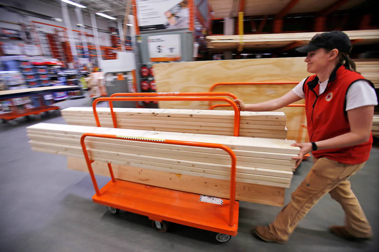 Home Depot 桌布 壁紙 — 一名身穿紅色背心的工人推著裝滿木板的橙色手推車，穿過繁忙的五金店通道。