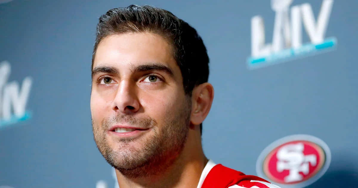 Jimmy Garoppolo 桌布 壁紙 — 一名身穿紅色舊金山49人隊球衣的男子，在藍色背景前帶有LAIV標誌的特寫肖像。
