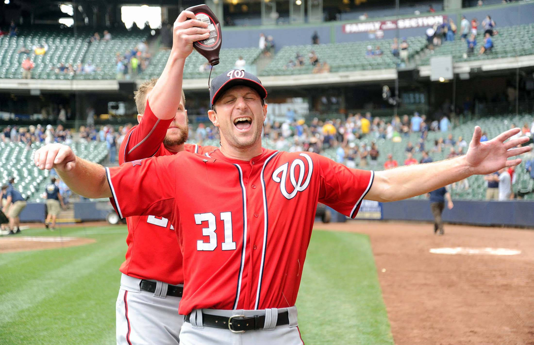 Max Scherzer 桌布 壁紙 — 一名身穿紅色華盛頓國民隊31號球衣的棒球運動員在陽光明媚的球場上慶祝勝利，隊友將醬汁倒在他的頭上。