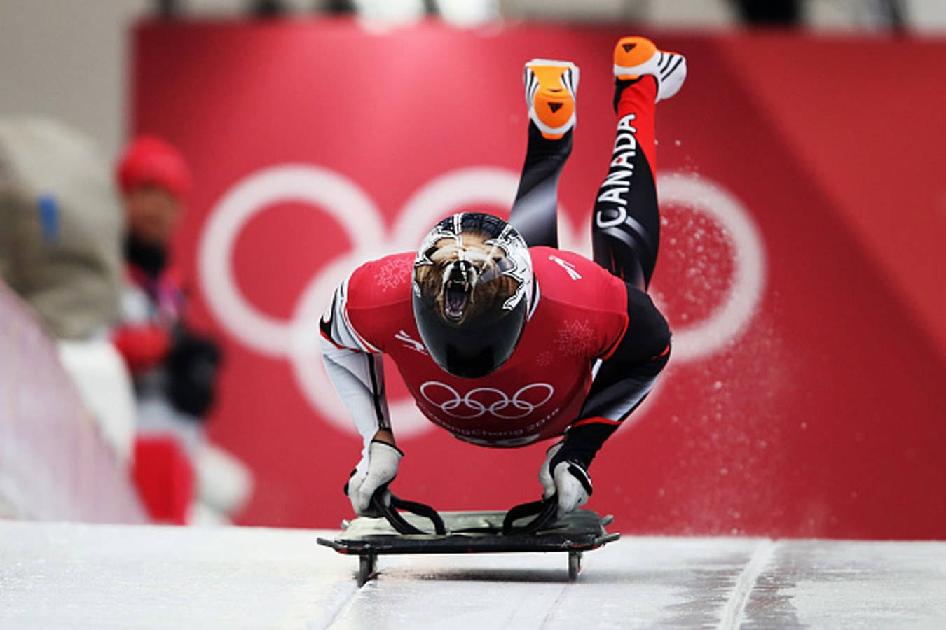 Olympics 桌布 壁紙 — 一名身穿紅色裝備的加拿大雪車運動員在比賽中途，雙腿踢起，以紅色奧運背景慶祝。