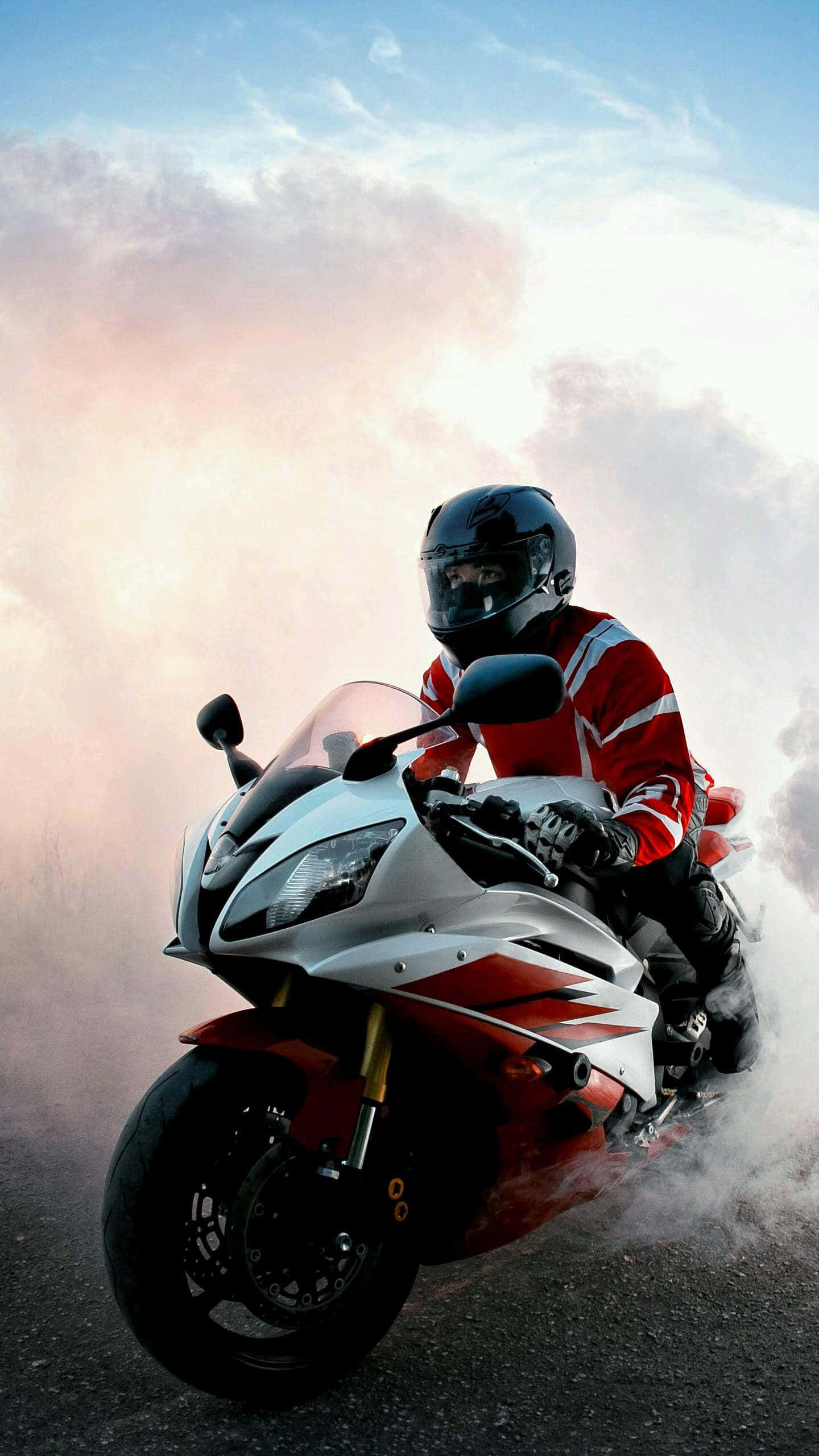 Superbike 桌布 壁紙 — 一名身穿紅色裝備的摩托車手在運動型摩托車上傾斜入彎，揚起煙霧，背景是陰天。