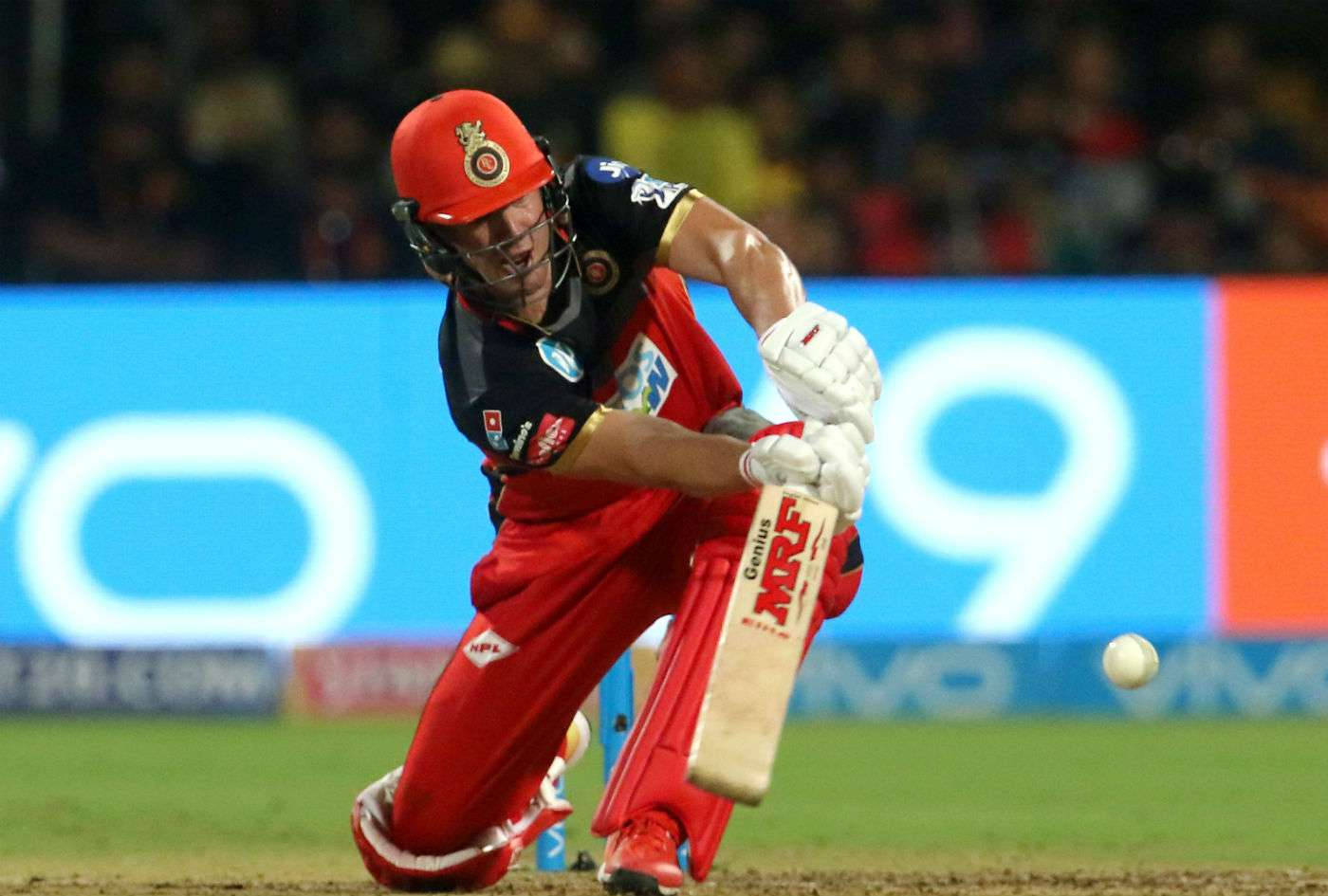 royal challengers bangalore 桌布 壁紙 — 一名身穿紅色裝備的板球擊球手在夜間比賽中，在球場燈光下揮動球棒擊球。