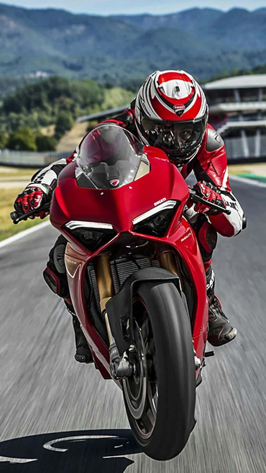 Superbike 桌布 壁紙 — 一名身穿紅色裝備的騎士在賽道上騎著鮮紅色運動機車轉彎，背景是模糊的綠色山丘。