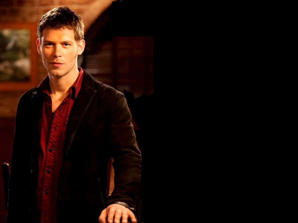 Vampire Diaries 桌布 壁紙 — 一名身穿紅色襯衫和深色外套的男子站在光線昏暗的房間中，溫暖的燈光在他的臉上投下陰影。