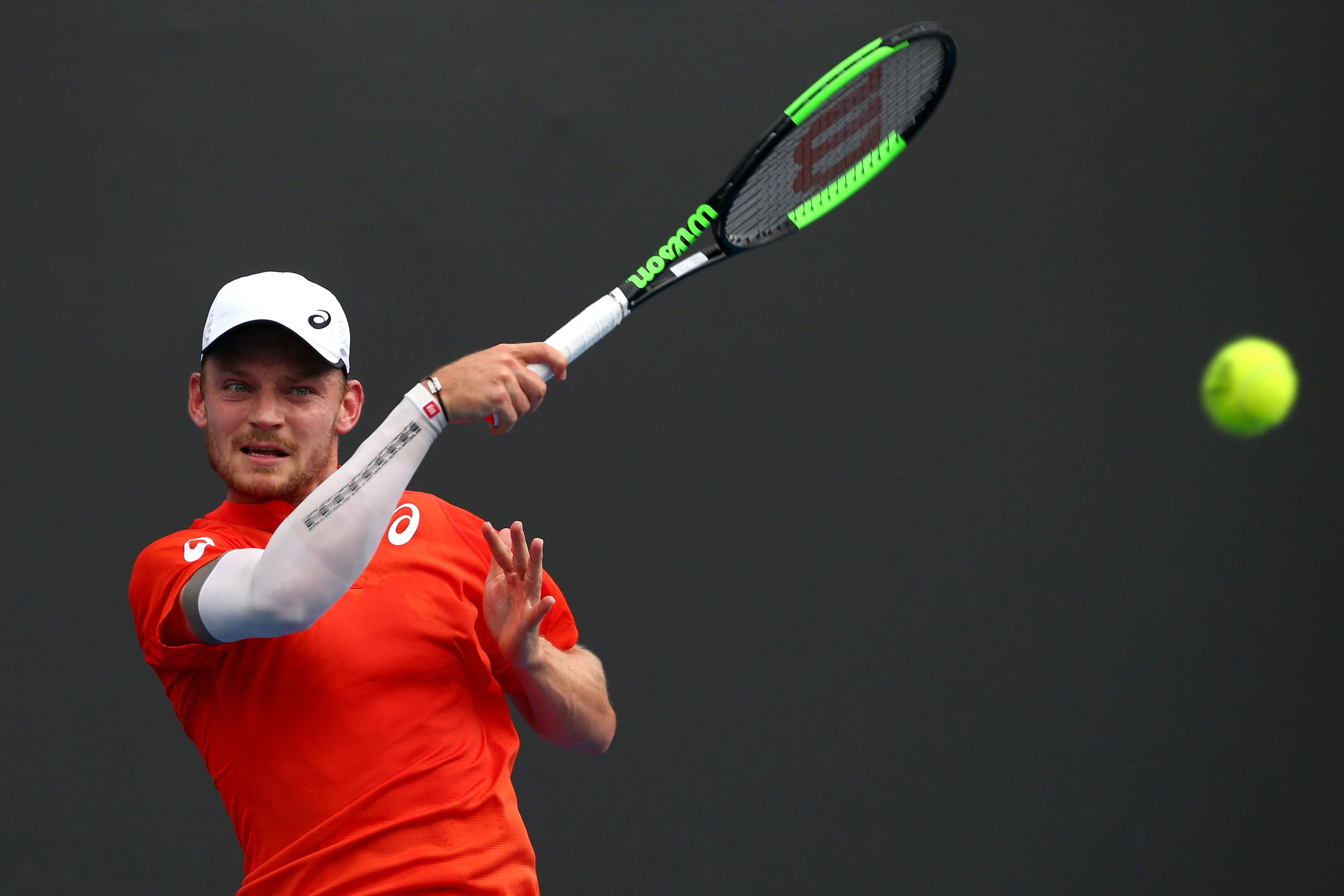 Tennis 桌布 壁紙 — 一名身穿紅色襯衫和白色帽子的男性網球運動員，在深色背景下揮動綠色和黑色的球拍擊打明亮的黃色網球。