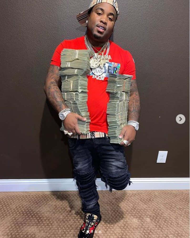 Rappers 桌布 壁紙 — 一名身穿紅色襯衫和破洞牛仔褲的男子在室內站立，穿著一疊疊現金製成的背心和閃亮珠寶。