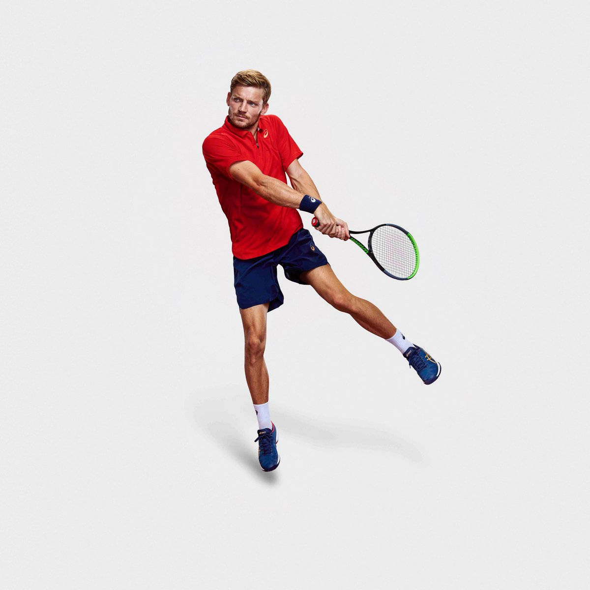 Tennis 桌布 壁紙 — 一名身穿紅色襯衫和藍色短褲的男性網球運動員在半空中跳躍，對著純白色背景揮動球拍。