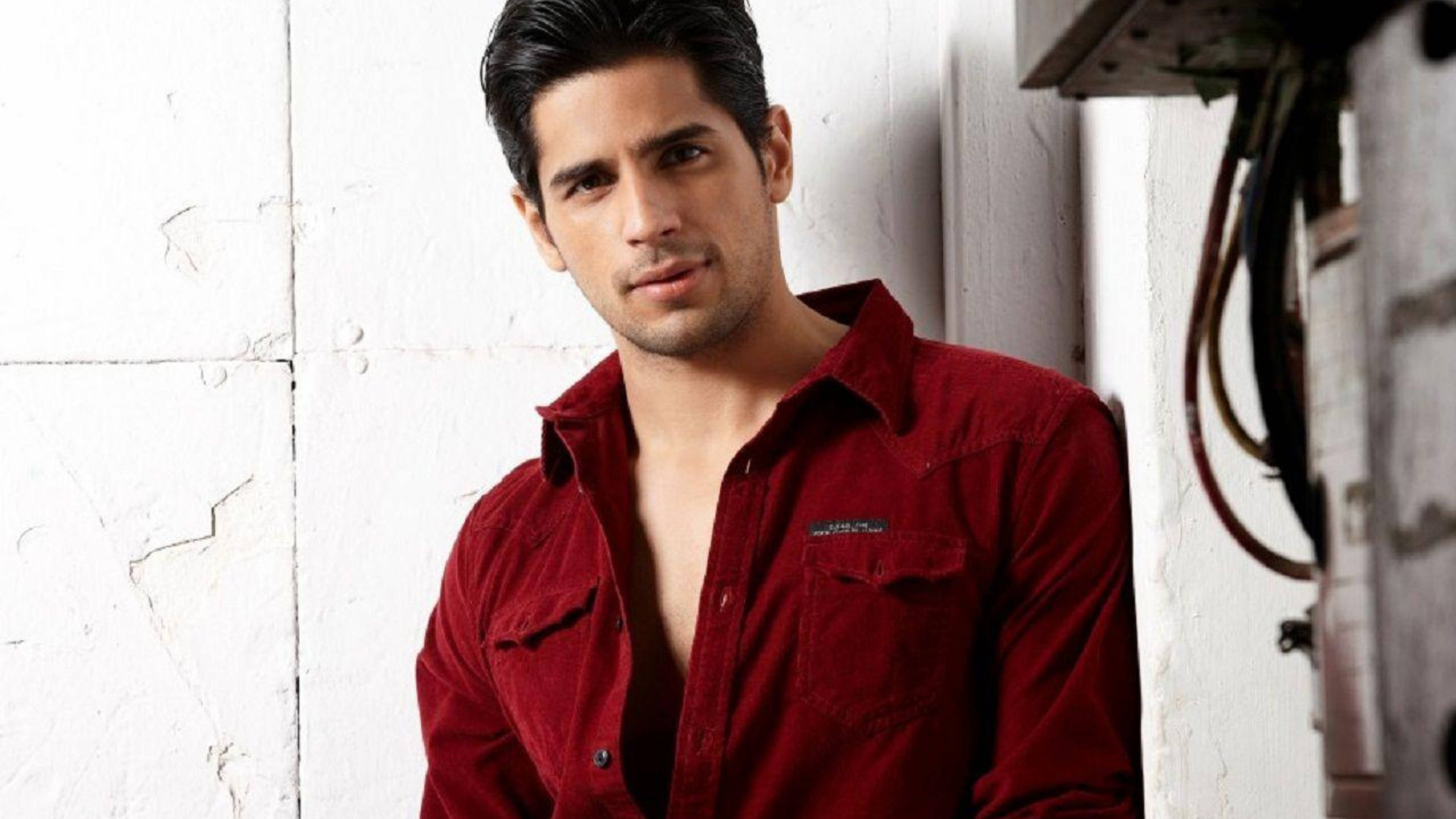 Sidharth Malhotra 桌布 壁紙 — 一名身穿紅色襯衫的男子靠在一面風化的白色牆壁上，附近有裸露的電線。