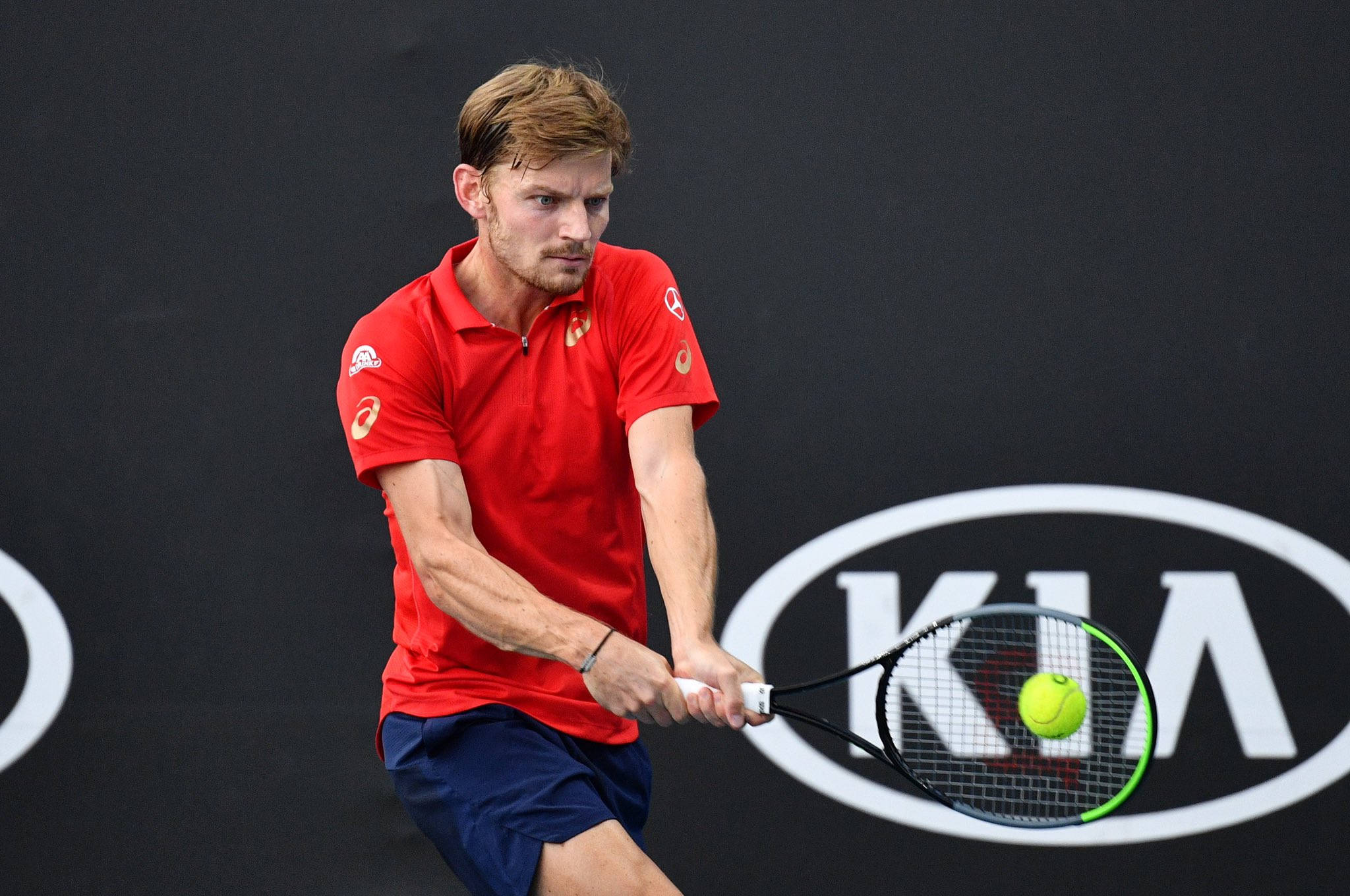 Tennis 桌布 壁紙 — 一名身穿紅色襯衫的男網球運動員揮動球拍，將一個亮黃色的網球擊向帶有Kia標誌的黑色牆壁。