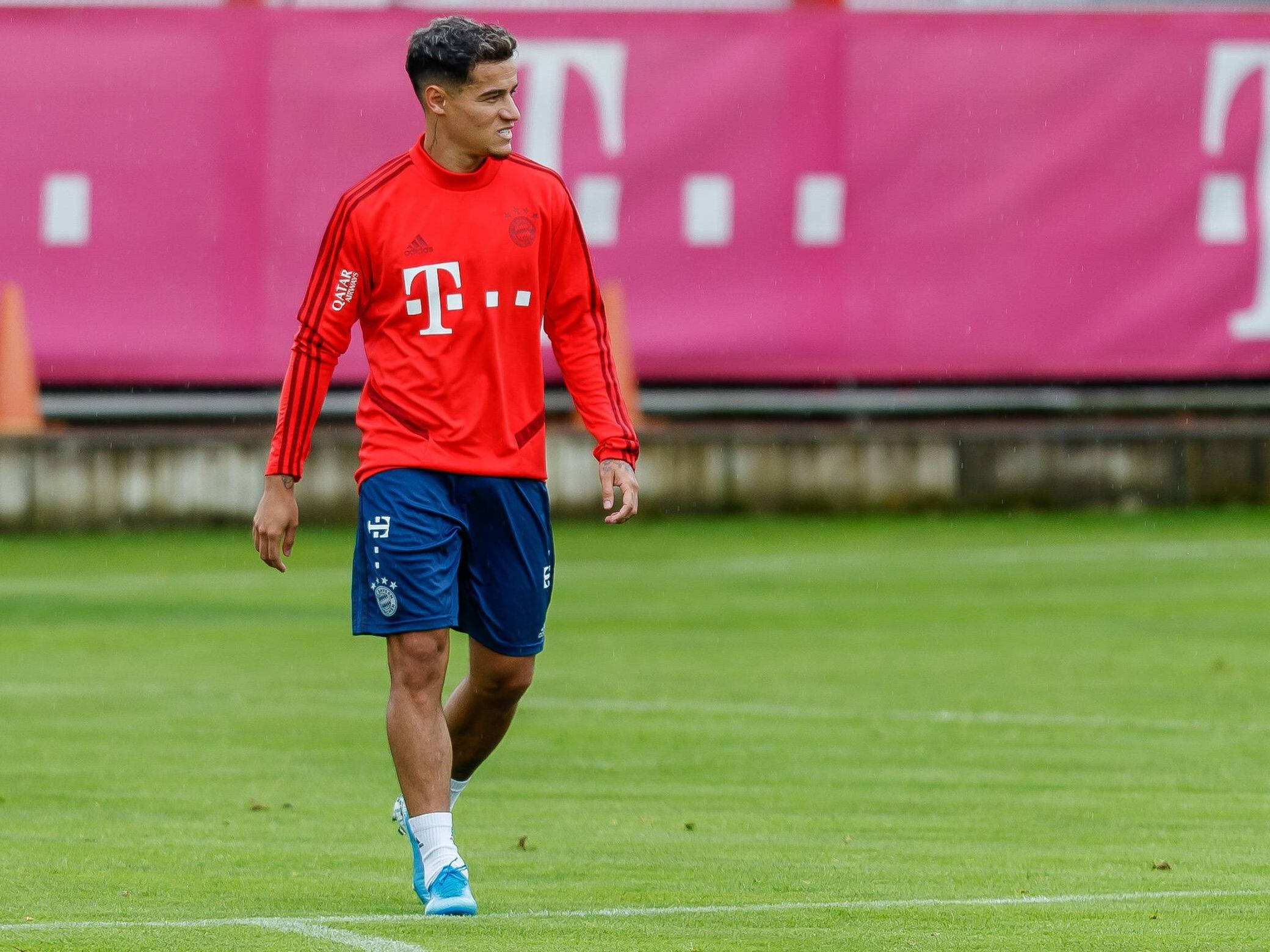Coutinho 桌布 壁紙 — 一名身穿紅色訓練裝備的足球運動員走過綠色球場，背景有粉紅色的T-Mobile橫幅。