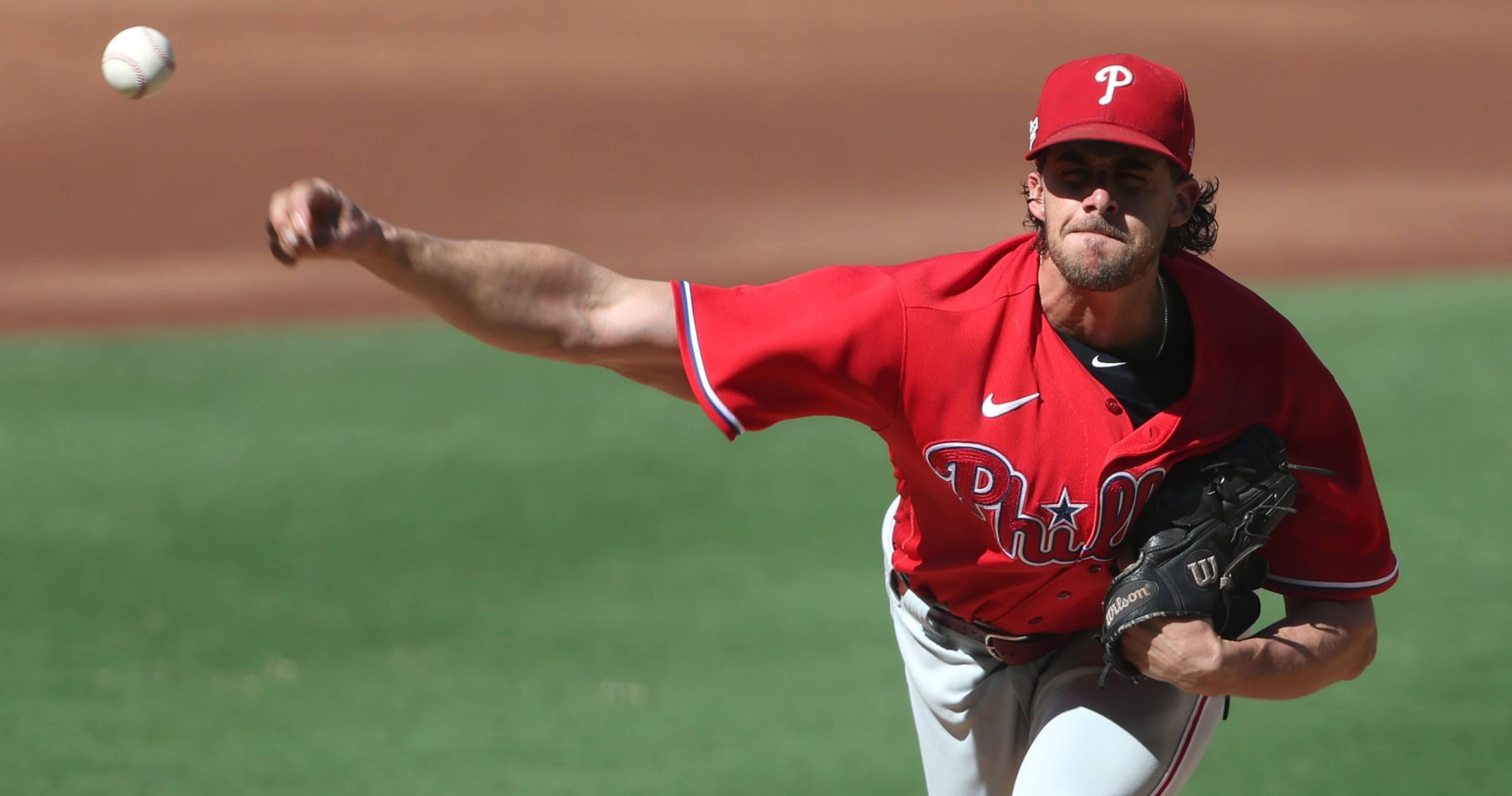 Phillies 桌布 壁紙 — 一名身穿紅色費城球衣的棒球投手，在陽光明媚、綠草如茵、泥土棕色的球場上投球。