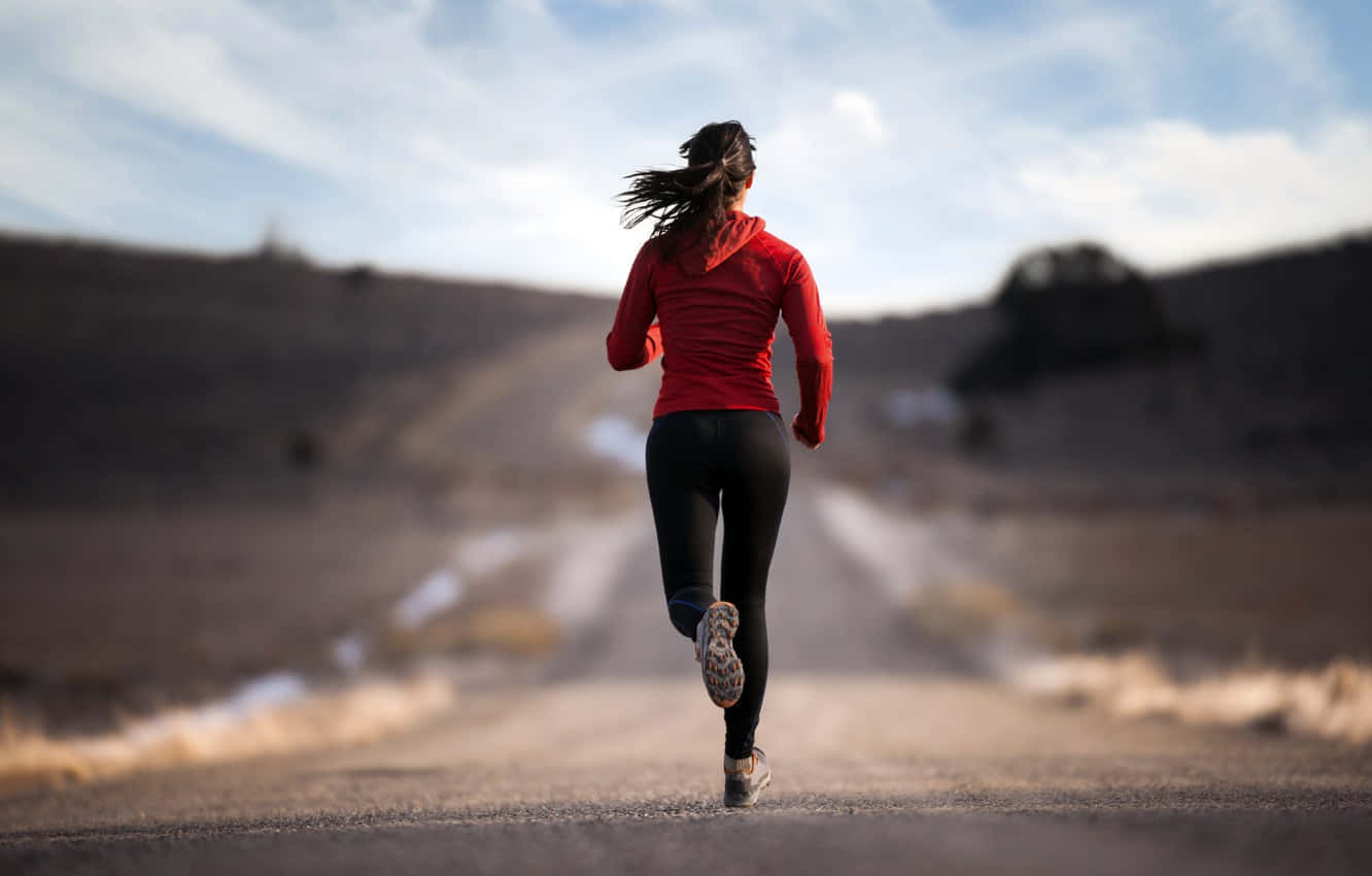 Fitness 桌布 壁紙 — 一名身穿紅色連帽衫的女子在晴朗的天空下，獨自沿著一條塵土飛揚的道路跑過一片貧瘠的風景。