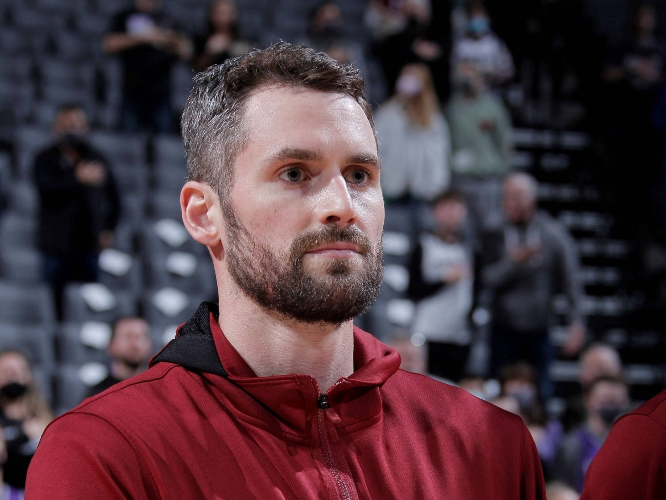 Kevin Love 桌布 壁紙 — 一名身穿紅色連帽衫的專注籃球運動員在比賽中凝視著，背景是模糊的觀眾。