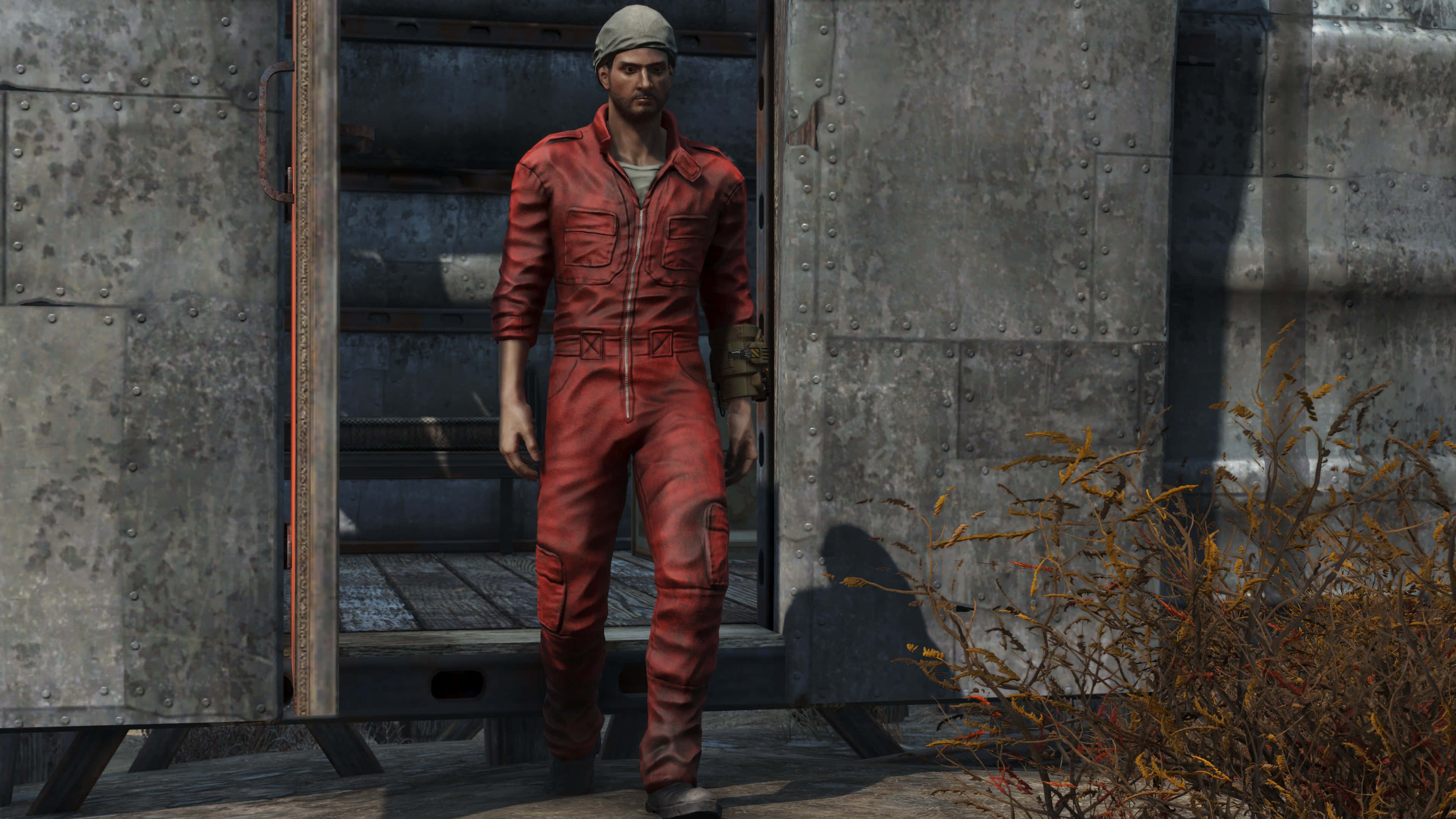 Fallout 4 The Capital Wasteland 桌布 壁紙 — 一名身穿紅色連身衣的男子從一扇生鏽的金屬門走進荒涼的工業廢墟。
