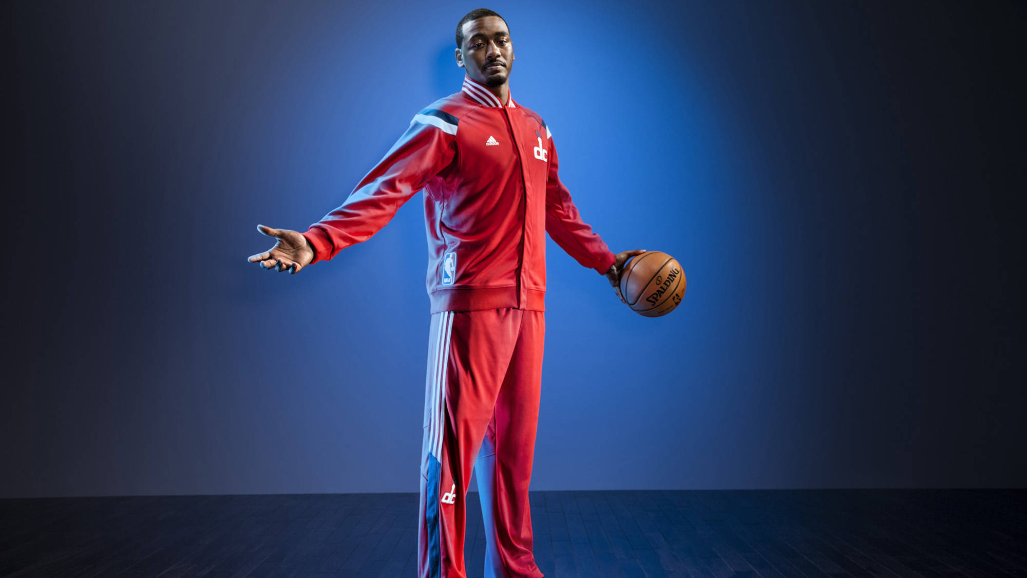 John Wall 桌布 壁紙 — 一名身穿紅色運動服的籃球運動員自信地站在藍色漸變工作室背景前，手持籃球。