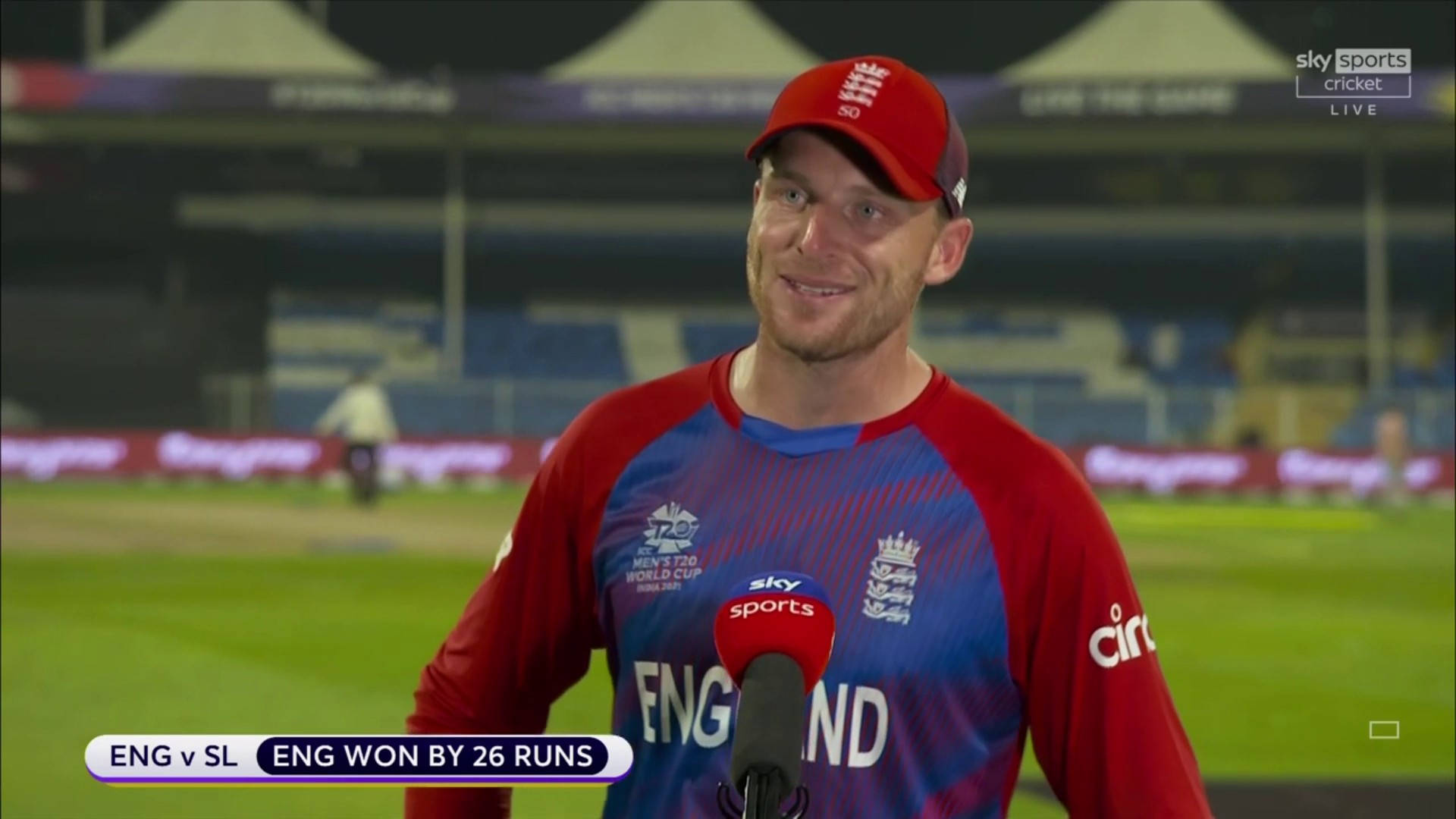 jos buttler 桌布 壁紙 — 一名身穿紅藍球衣的英格蘭板球運動員在球場燈光下接受賽後採訪時微笑。