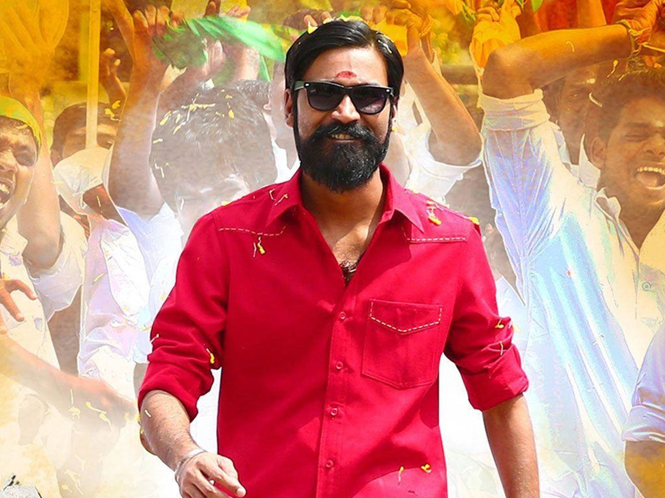 Dhanush 桌布 壁紙 — 一名身穿紅衫和太陽眼鏡的男子在節日慶祝活動中，彩色粉末在他周圍飛舞，他自信地微笑。