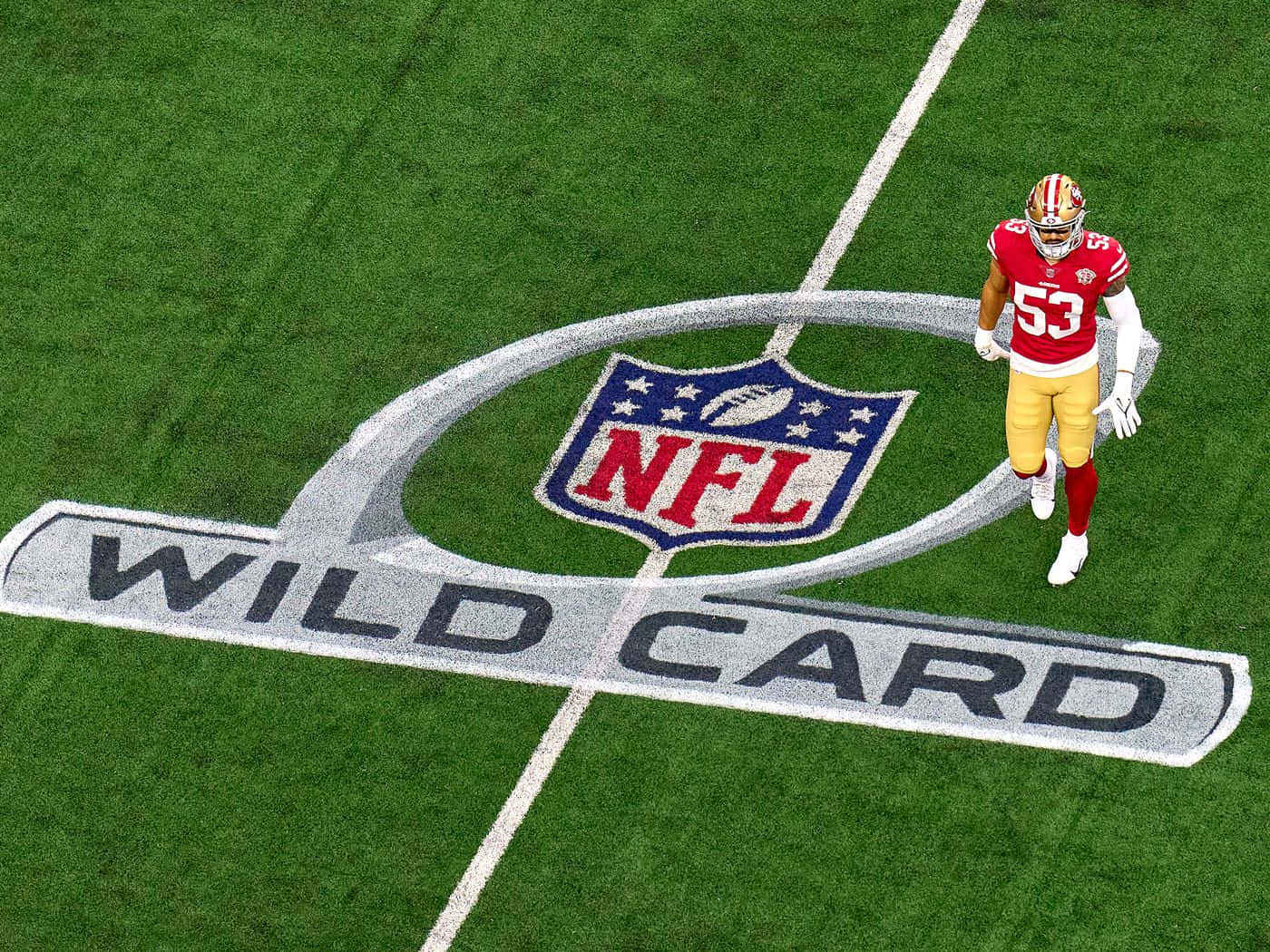 運動 桌布 壁紙 — 一名身穿紅金球衣的NFL球員在綠色球場上走過一個巨大的「WILD CARD」標誌。