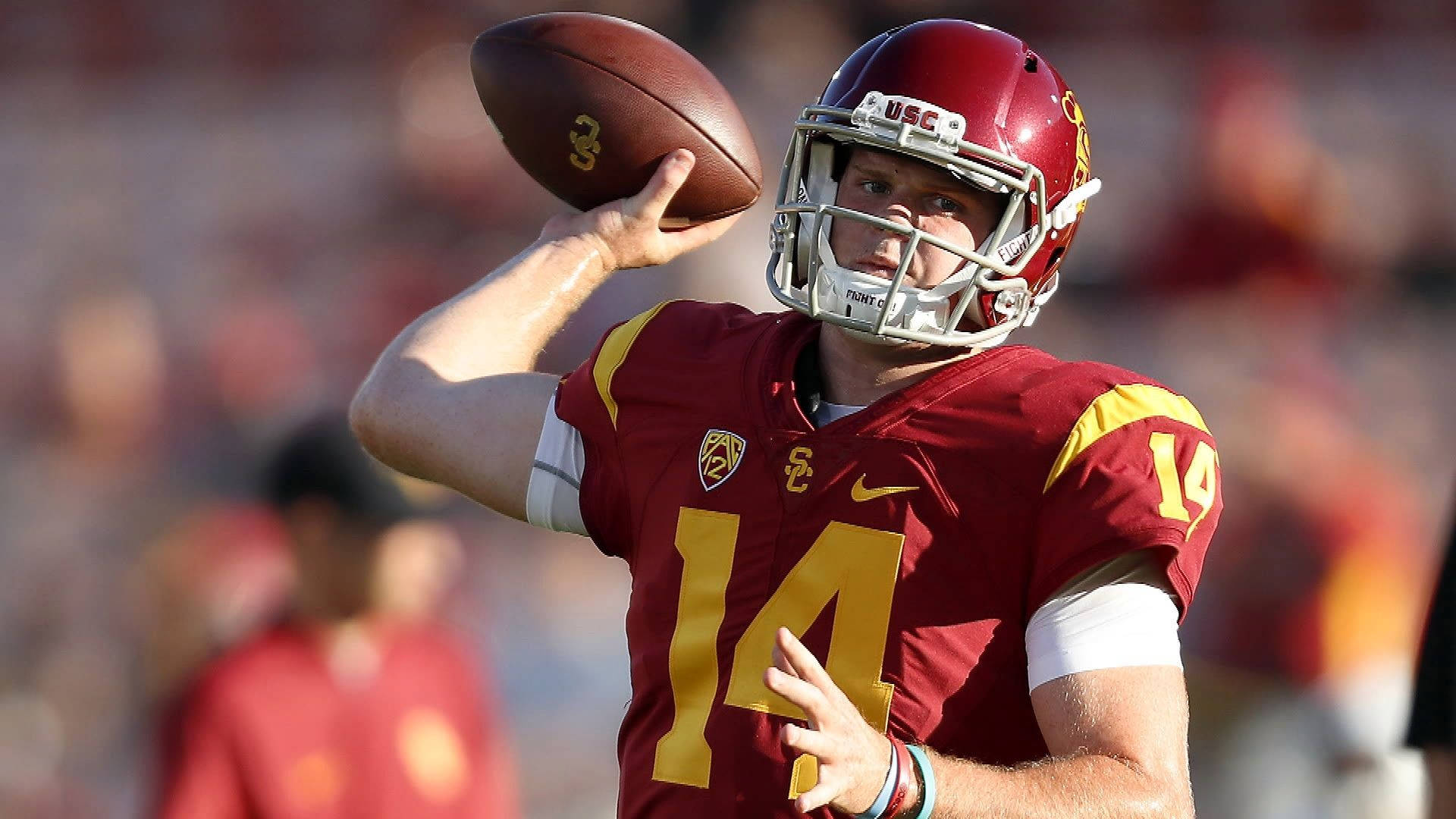 Usc Football 桌布 壁紙 — 一名身穿紅金色制服的USC足球四分衛在陽光明媚的比賽中準備投球。