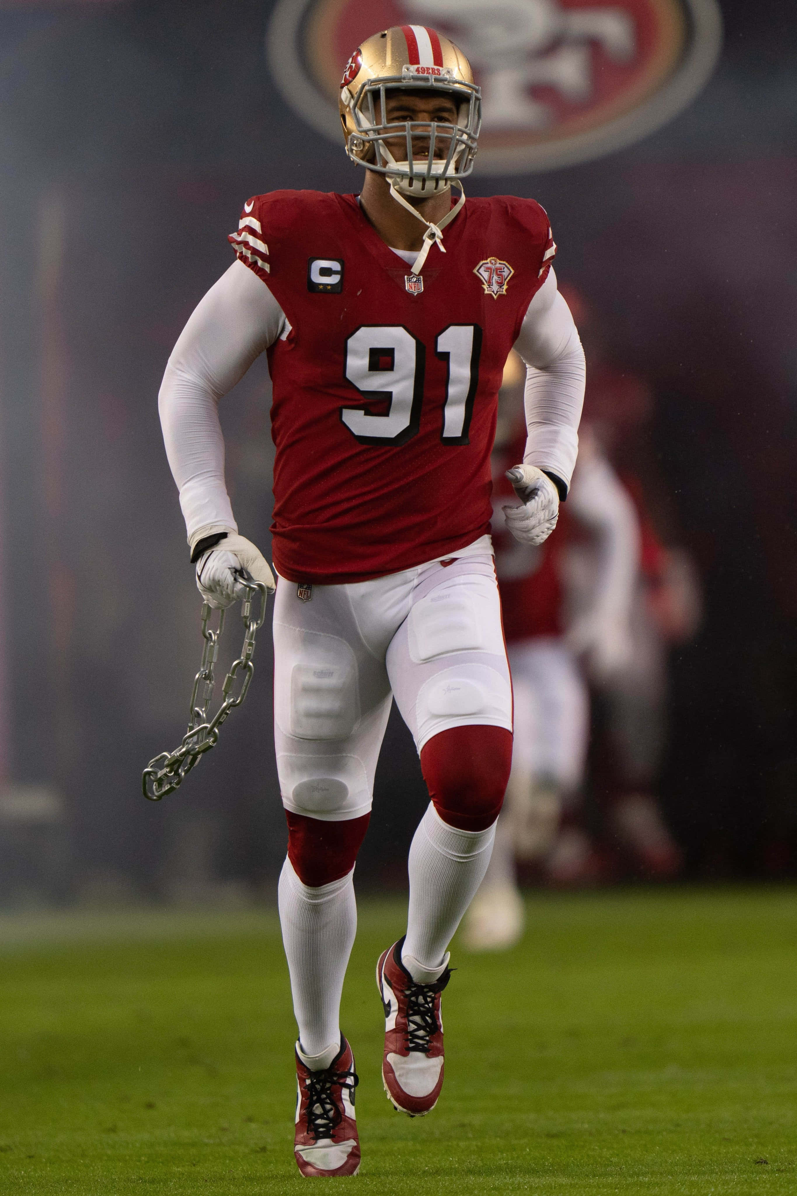 San Francisco 49ers 桌布 壁紙 — 一名身穿紅金色球衣的舊金山四九人美式足球員在綠色球場上拿著他的鏈條奔跑。