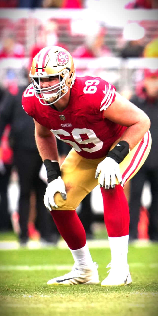 Mike Mcglinchey 桌布 壁紙 — 一名身穿紅金色球衣的舊金山四九人美式足球員在綠色球場上激烈蹲伏。