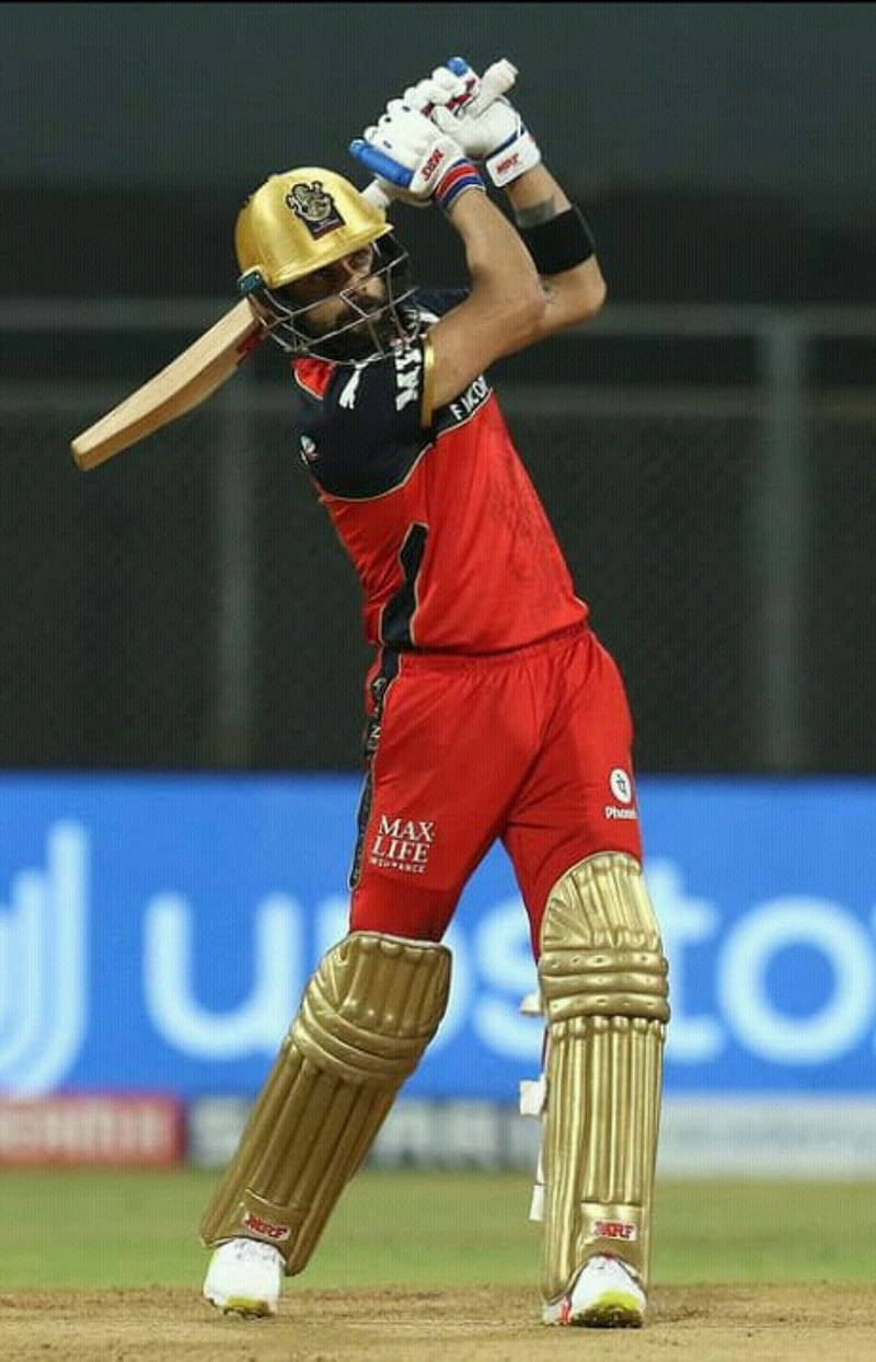 royal challengers bangalore 桌布 壁紙 — 一名身穿紅金裝備的板球擊球手在體育場燈光下強力揮動球棒。