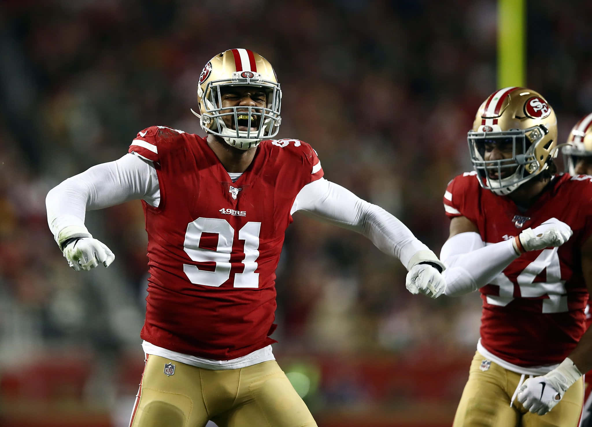 San Francisco 49ers 桌布 壁紙 — 一名身穿紅金配色球衣的舊金山49人美式足球員在夜間燈光球場上張開雙臂慶祝。