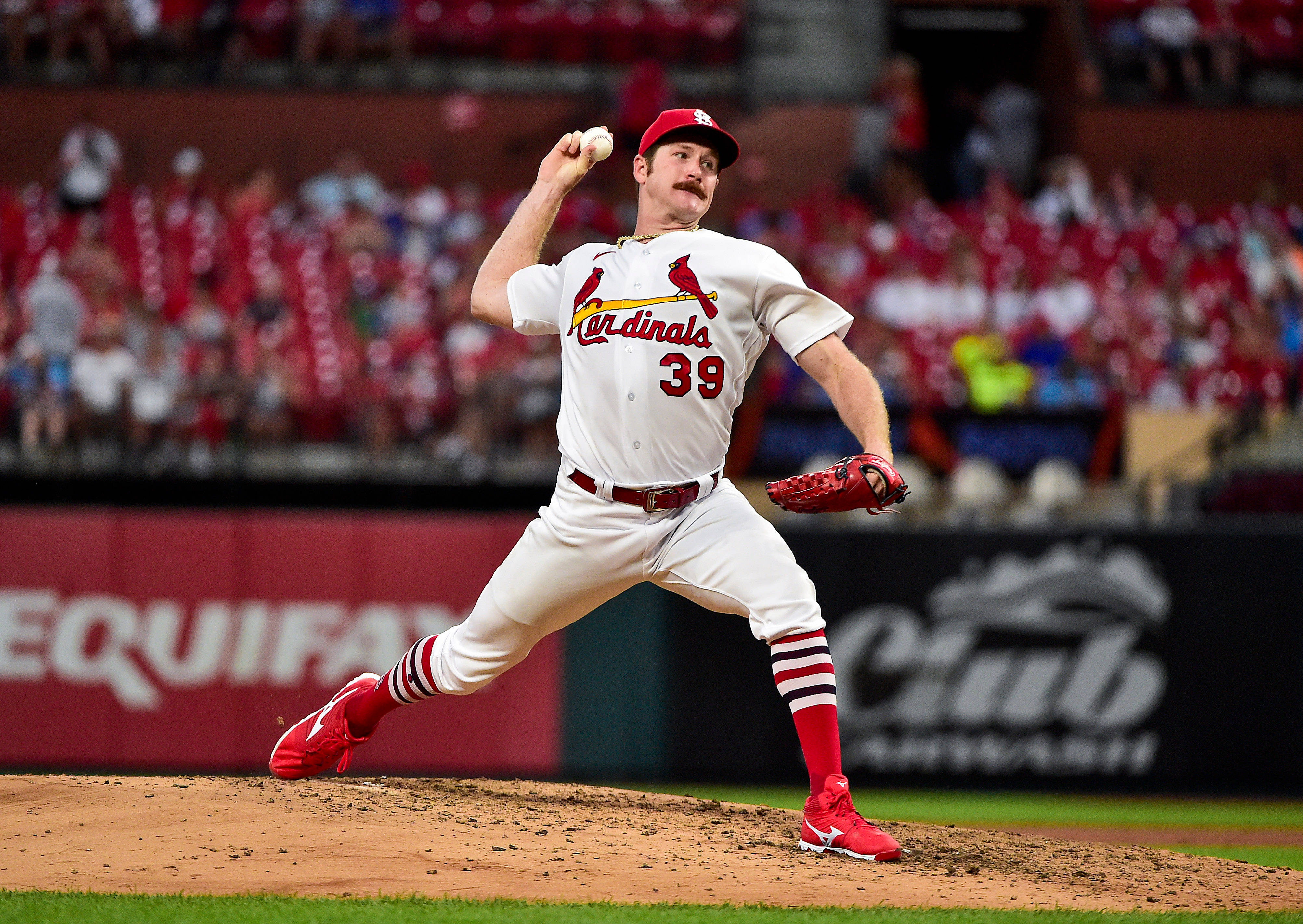 St Louis Cardinals 桌布 壁紙 — 一名身穿紅雀隊球衣的棒球投手在泥土投手丘上投球，身後有模糊的人群坐在紅色座位上。