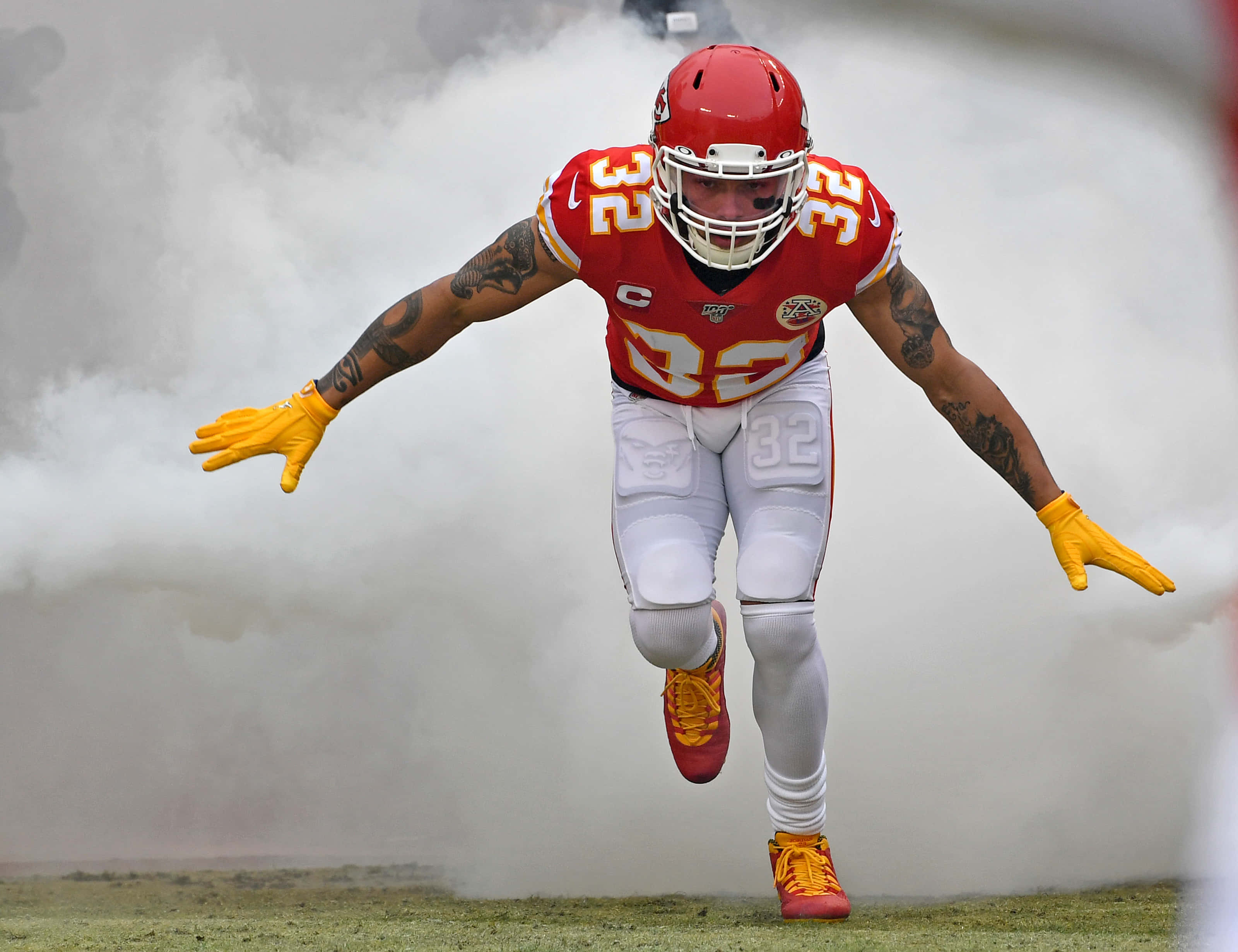 Tyrann Mathieu 桌布 壁紙 — 一名身穿紅黃球衣的足球員在草地上張開雙臂，躍過煙霧。