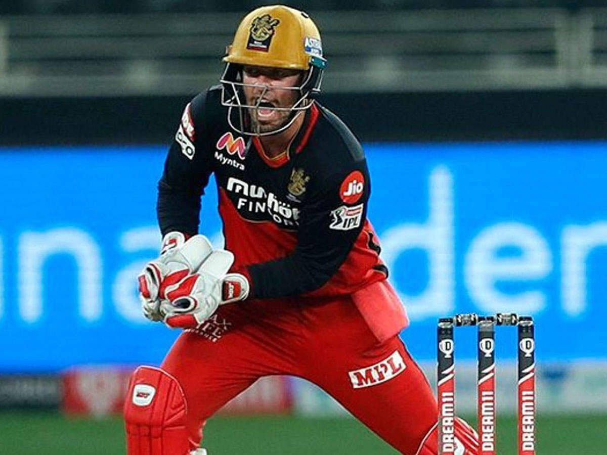 royal challengers bangalore 桌布 壁紙 — 一名身穿紅黑制服的板球擊球手在夜間比賽中向前衝刺，準備用球棒擊球。
