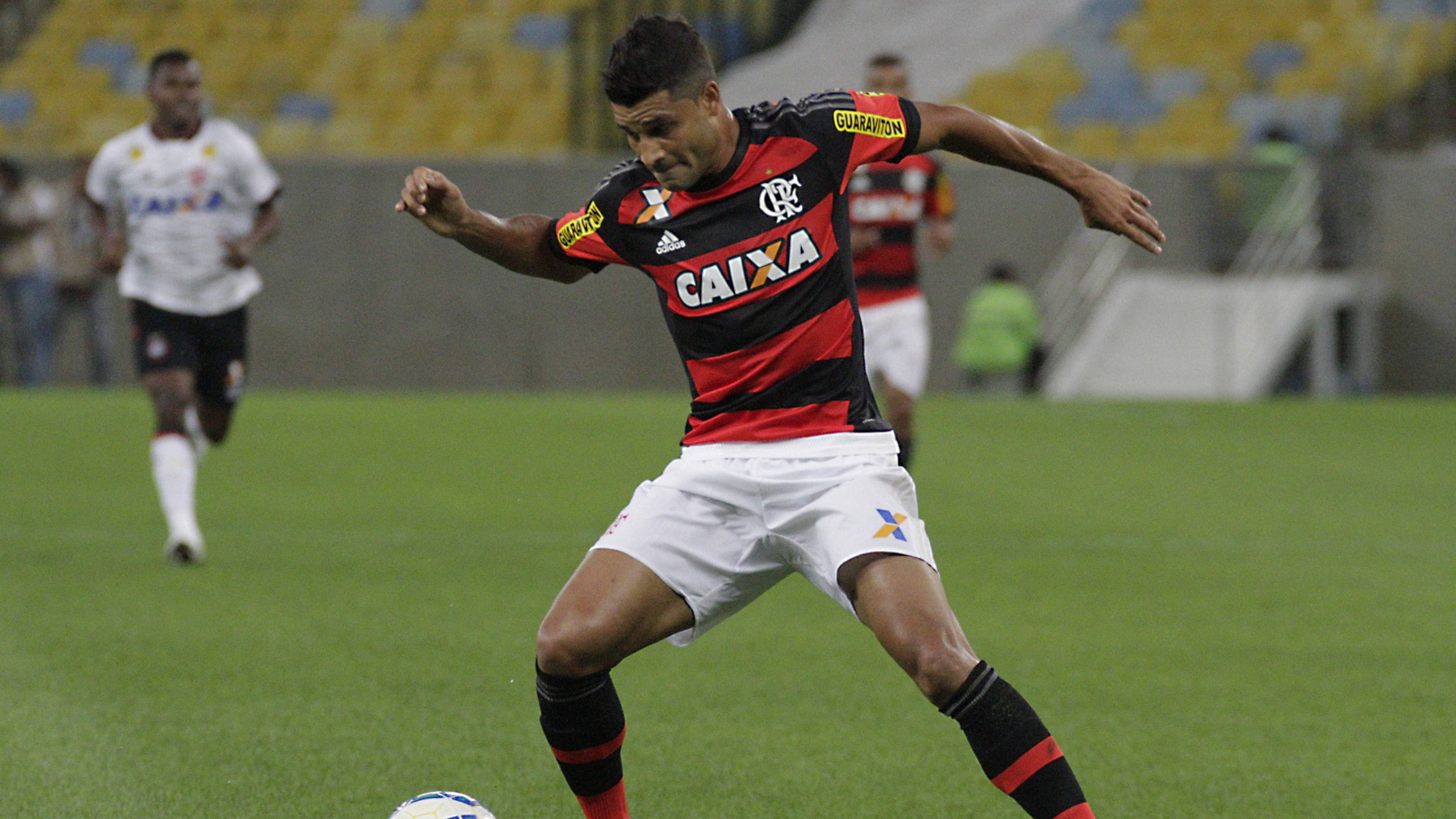 flamengo fc 桌布 壁紙 — 一名身穿紅黑條紋球衣的足球員在綠色球場上踢球，球場燈光下，黃色座位上的觀眾模糊不清。