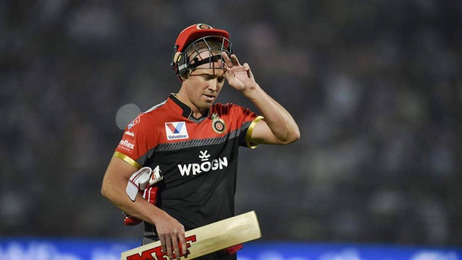 royal challengers bangalore 桌布 壁紙 — 一名身穿紅黑球衣的板球運動員在球場燈光下調整頭盔，同時手持球棒。