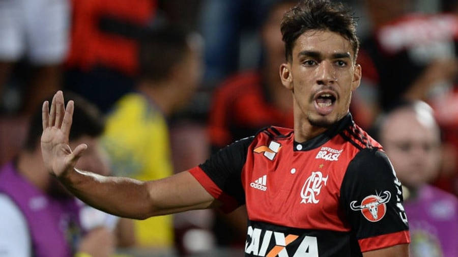 足球 桌布 壁紙 — 一名身穿紅黑球衣的足球員在夜間比賽中，於球場燈光下熱情地做手勢。