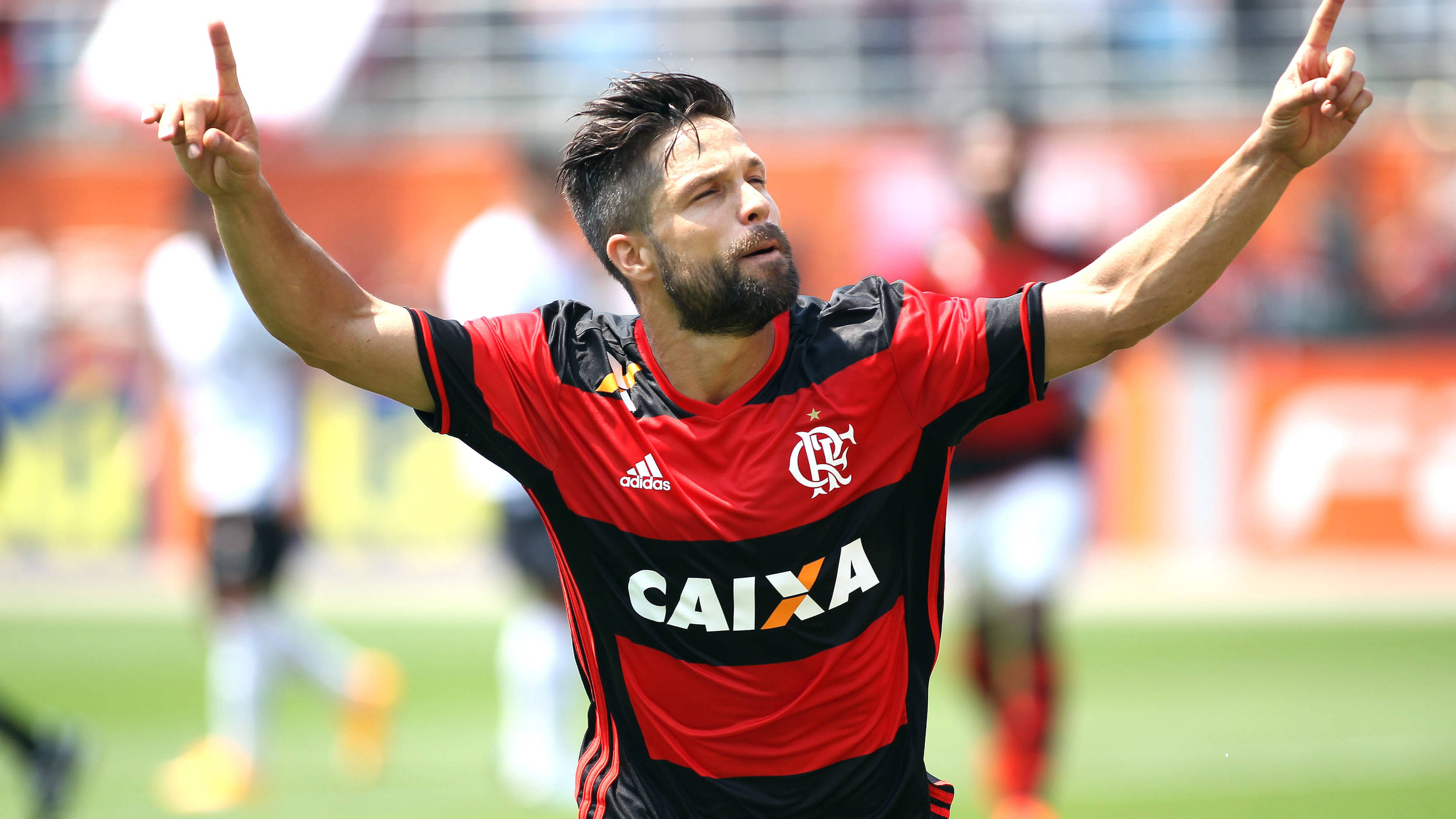 flamengo fc 桌布 壁紙 — 一名身穿紅黑球衣的足球員在陽光明媚的球場上高舉雙臂慶祝勝利。