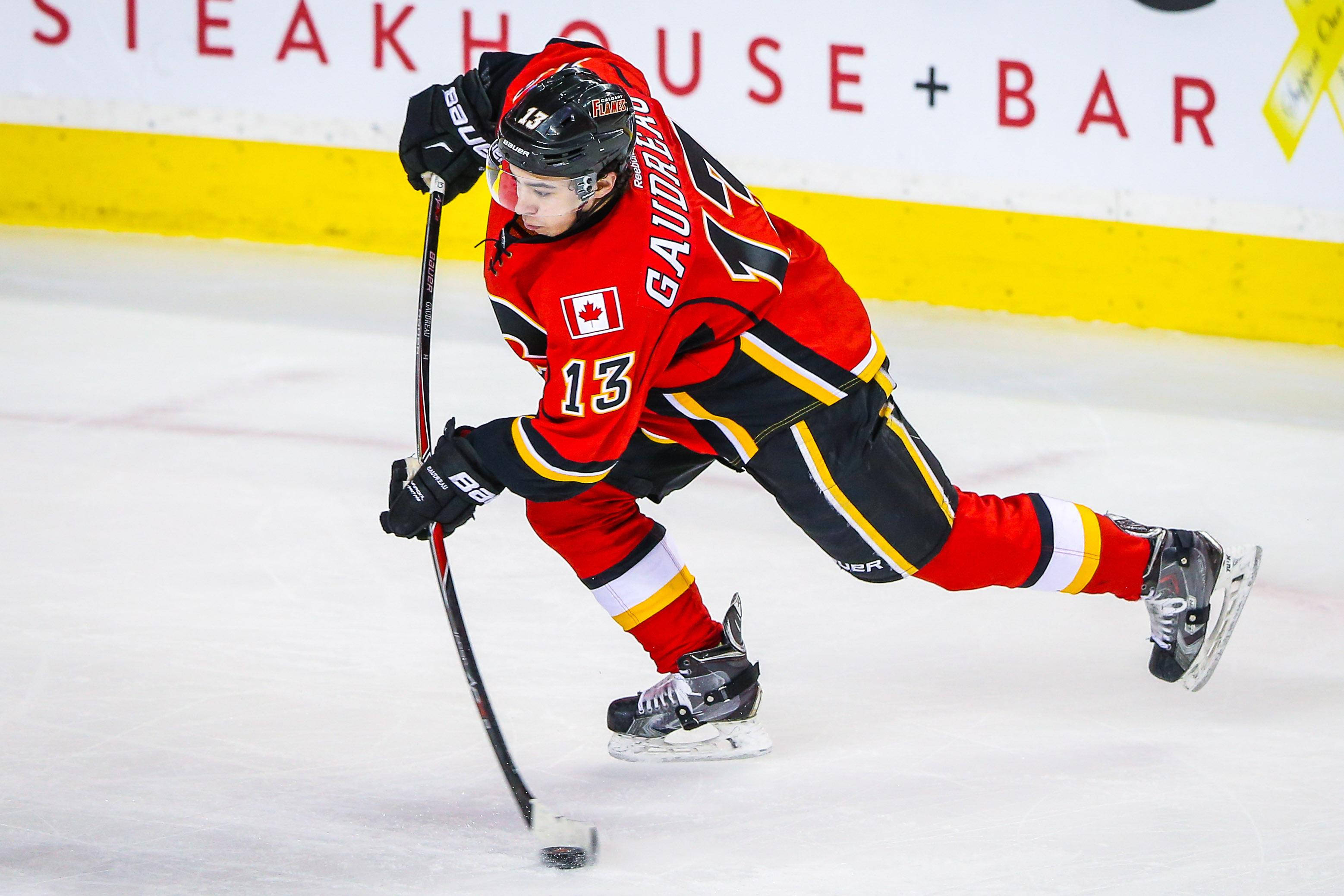 Johnny Gaudreau 桌布 壁紙 — 一名身穿紅黑色球衣的冰上曲棍球運動員在冰上低身彎腰，手持球棍專注於冰球比賽中。