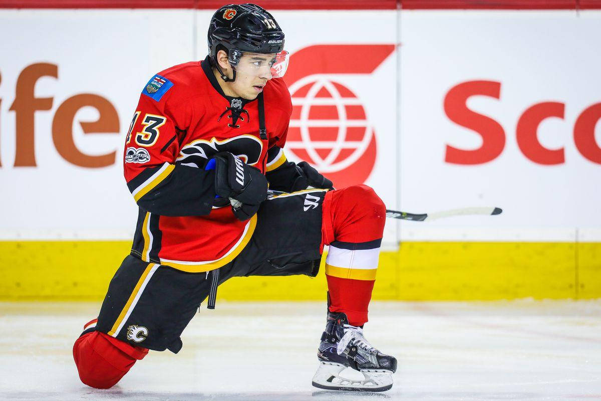Johnny Gaudreau 桌布 壁紙 — 一名身穿紅黑色裝備的冰上曲棍球運動員在比賽中低蹲在冰上，專注地握著球棍。