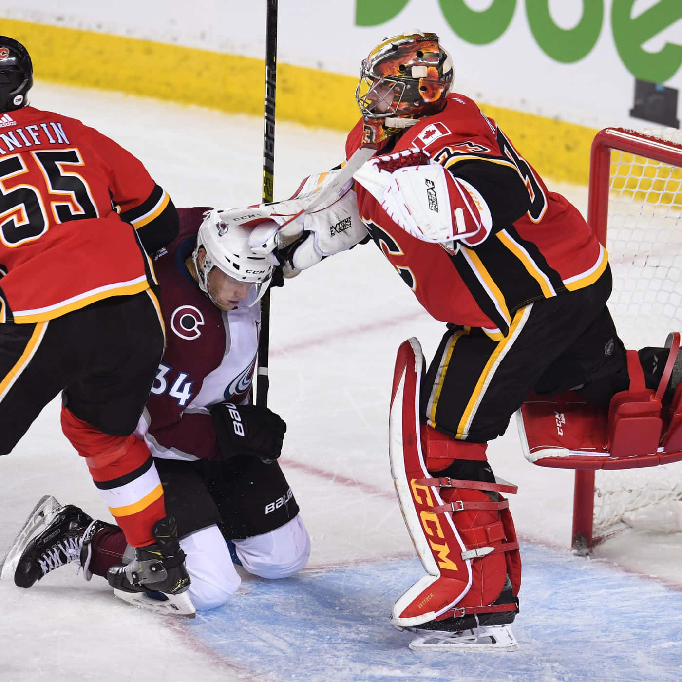Calgary Flames 桌布 壁紙 — 一名身穿紅黑色裝備的冰球守門員擋住射門，而一名身穿棗紅色球衣的對方球員在冰上向前推進。