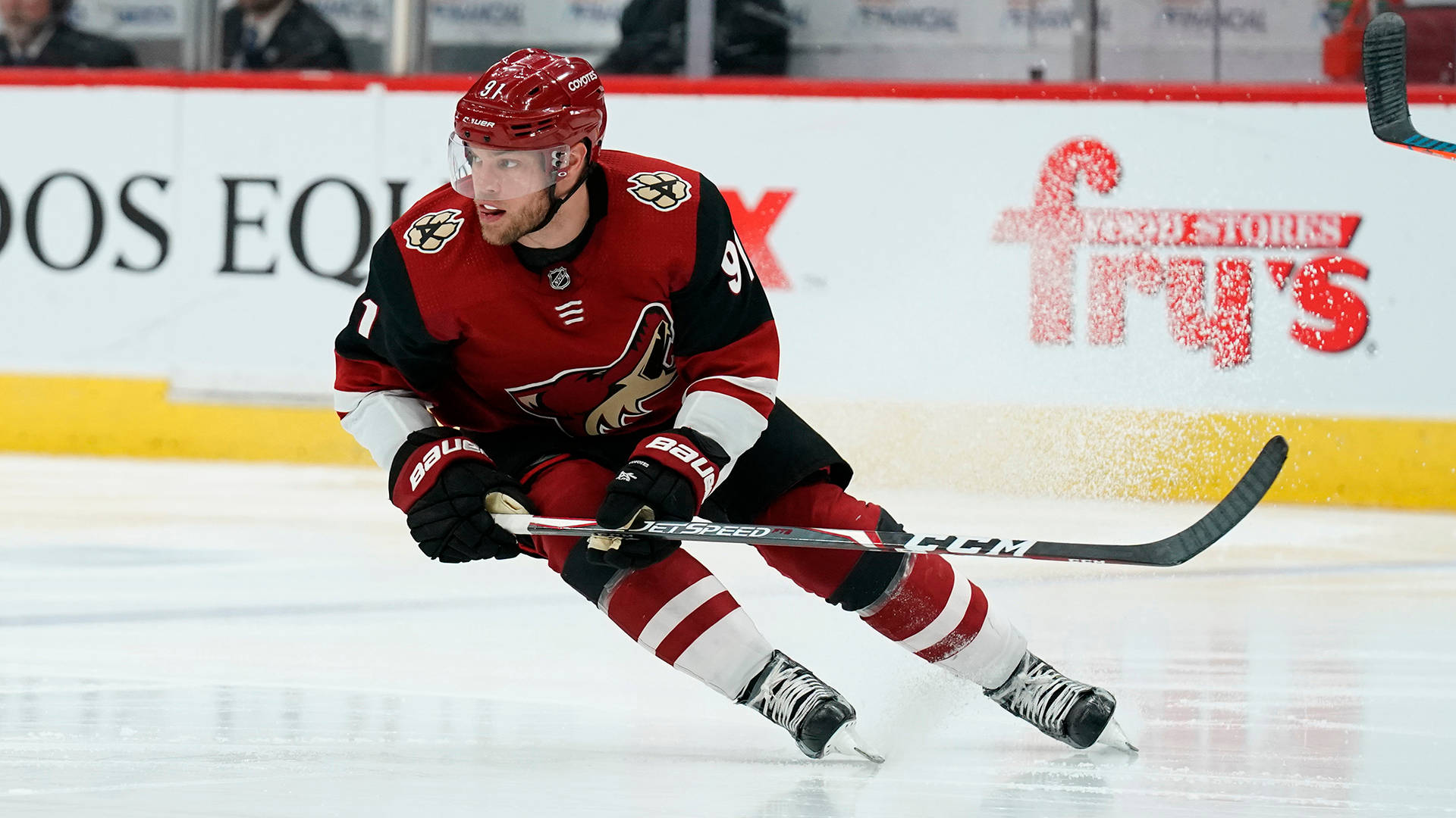 hockey 桌布 壁紙 — 一名身穿紅黑裝備的冰球運動員在冰上低身俯衝，手持球棍，身後有飛濺的水花。
