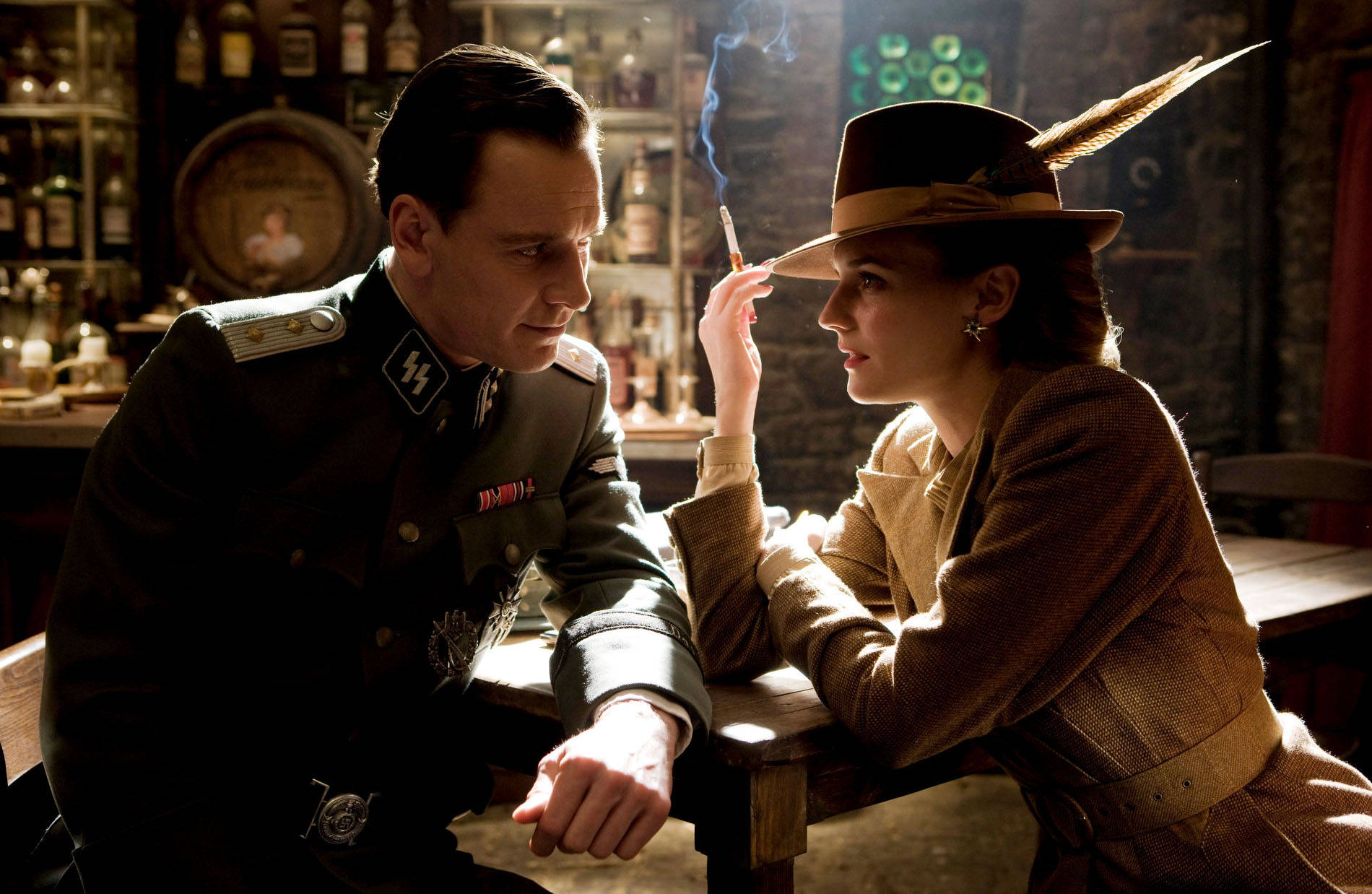 Inglourious Basterds 桌布 壁紙 — 一名身穿納粹制服的男人和一名戴著羽毛帽的女人，在燈光昏暗的酒吧裡，圍繞著一支香煙分享著緊張的時刻。