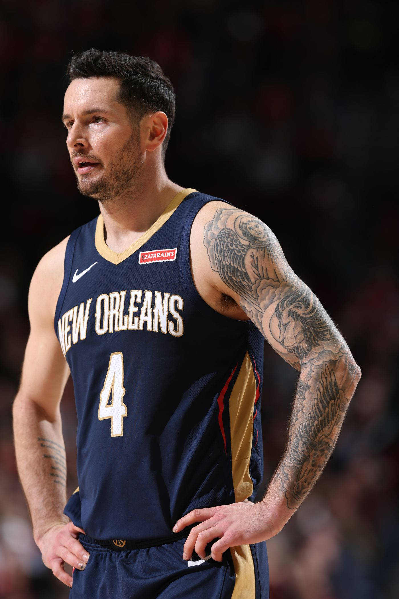 Jj Redick 桌布 壁紙 — 一名身穿紐奧良球衣的籃球運動員雙手叉腰，在場館燈光下展示精細的手臂刺青。