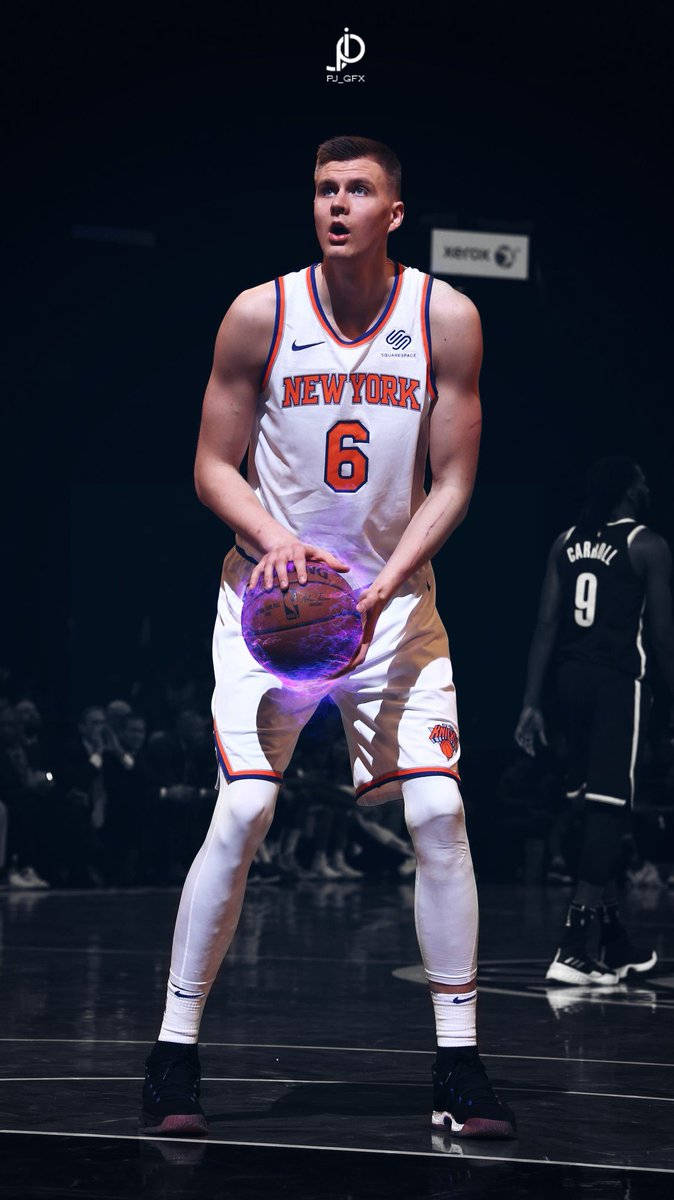 Kristaps Porzingis 桌布 壁紙 — 一名身穿紐約尼克隊球衣的籃球運動員在場館燈光下手持發光的紫色籃球。