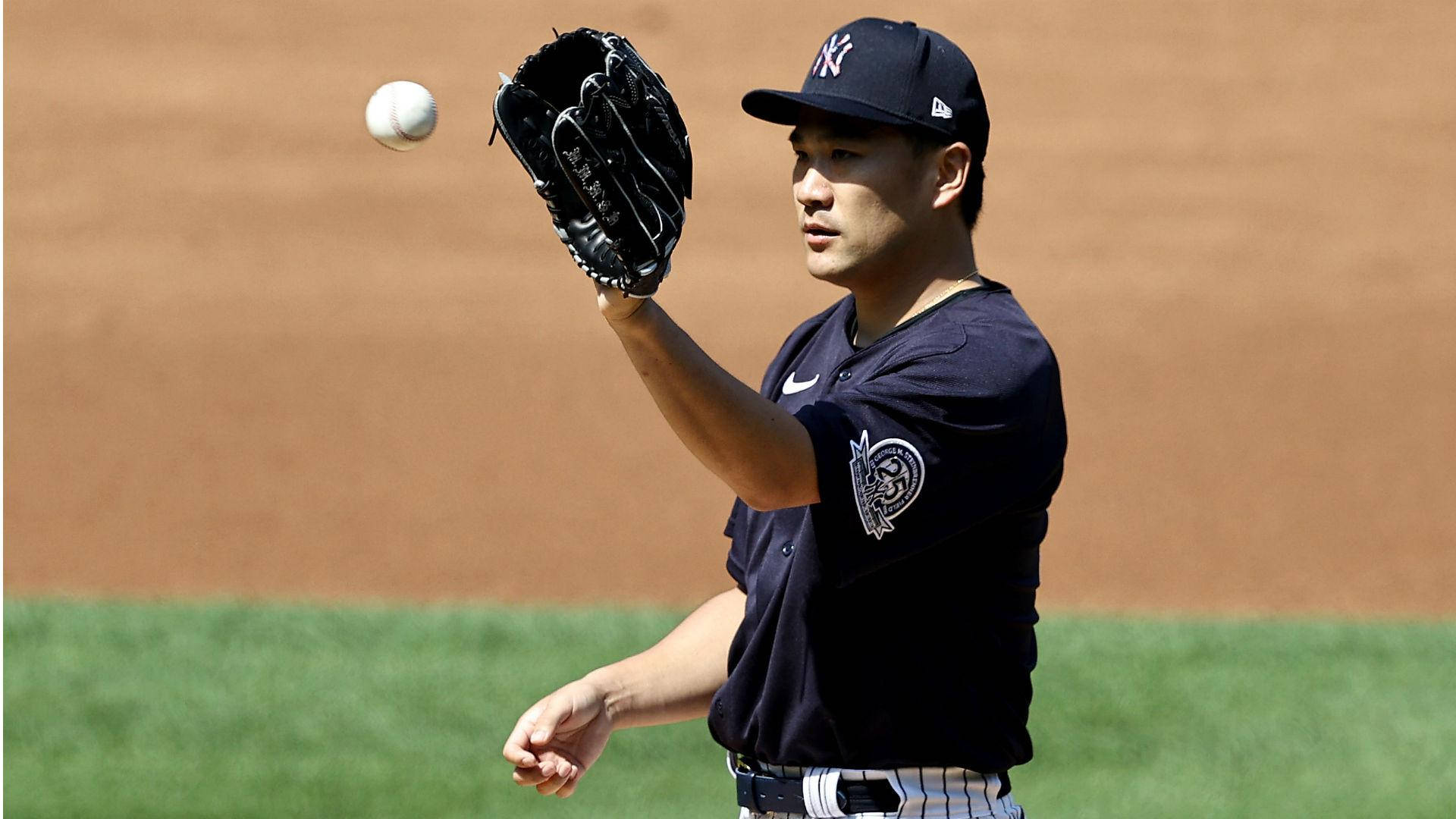 masahiro tanaka 桌布 壁紙 — 一名身穿紐約洋基隊球衣的棒球選手在陽光明媚的球場上用他的手套接住空中的球。