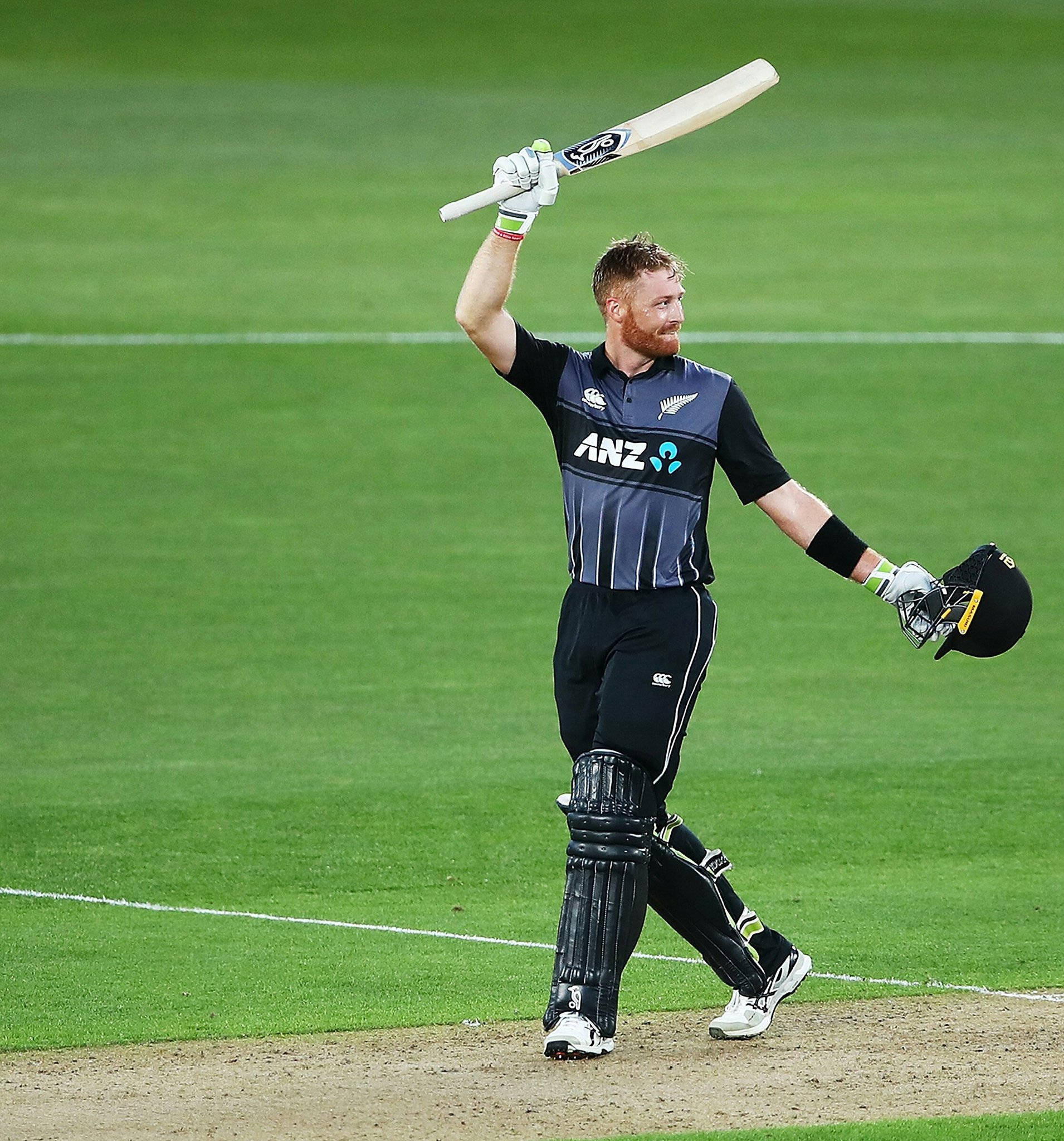 martin guptill 桌布 壁紙 — 一名身穿紐西蘭隊服的板球運動員在體育場燈光下，在充滿活力的綠色球場上高舉球棒慶祝。