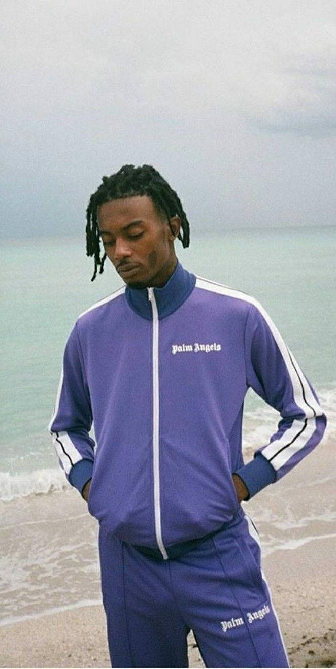 Carti 桌布 壁紙 — 一名身穿紫色 Palm Angels 運動服的男子站在霧氣瀰漫的海灘上，身後海浪翻滾。