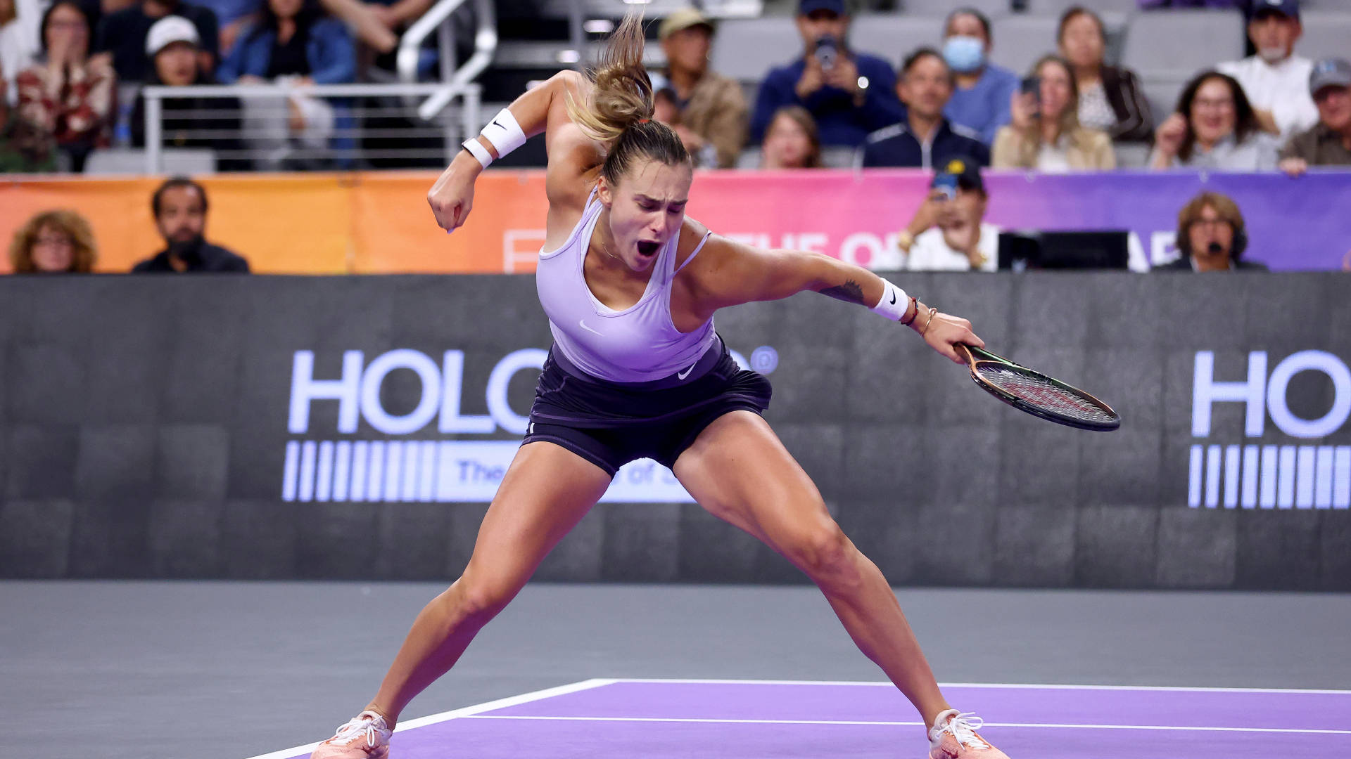 Aryna Sabalenka 桌布 壁紙 — 一名身穿紫色上衣和黑色短褲的女網球運動員在紫色球場上比賽時，專注地向前猛衝。