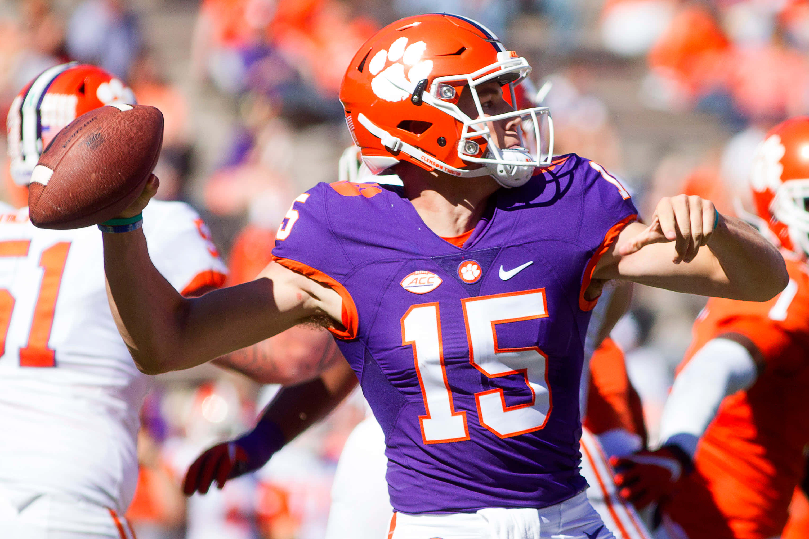 Clemson 桌布 壁紙 — 一名身穿紫色和橙色球衣的克萊姆森美式足球四分衛在明亮的日間比賽中準備投球。