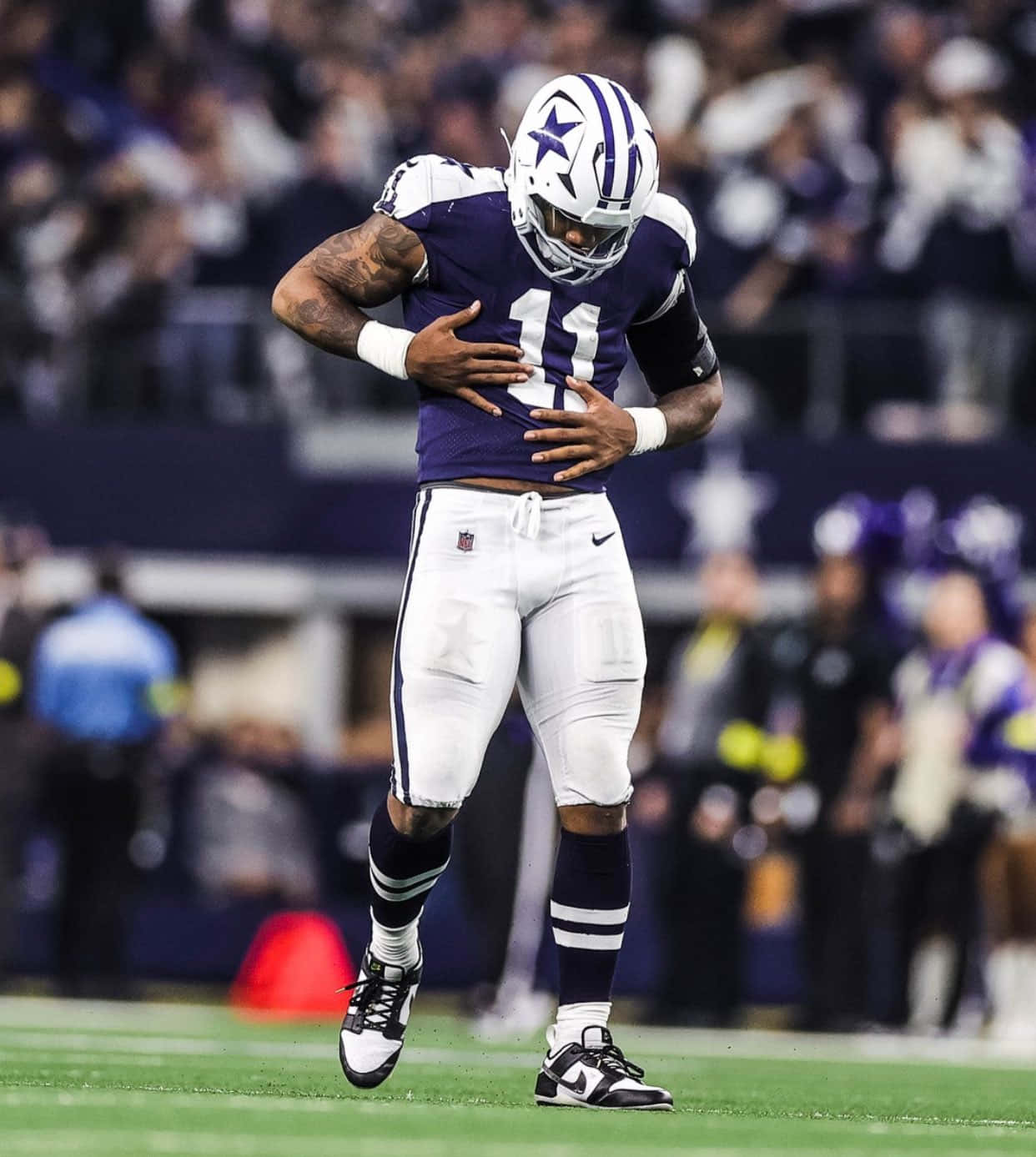 Dallas Cowboys Players 桌布 壁紙 — 一名身穿紫色和白色球衣的達拉斯牛仔隊美式足球員在球場燈光下比賽期間，雙手放在胸前站在場上。