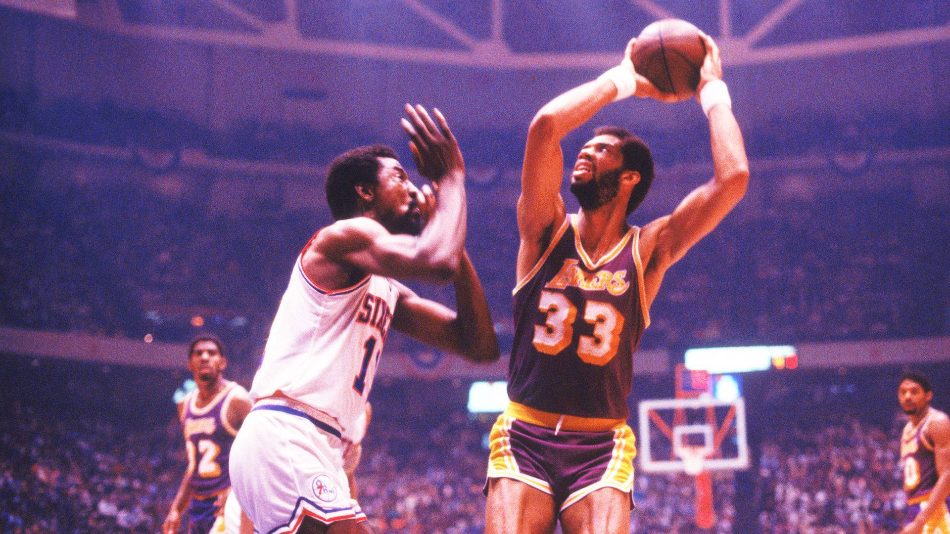 Kareem 桌布 壁紙 — 一名身穿紫色湖人球衣、背號33的籃球運動員跳起投籃，而一名身穿白色球衣的防守球員試圖封阻。