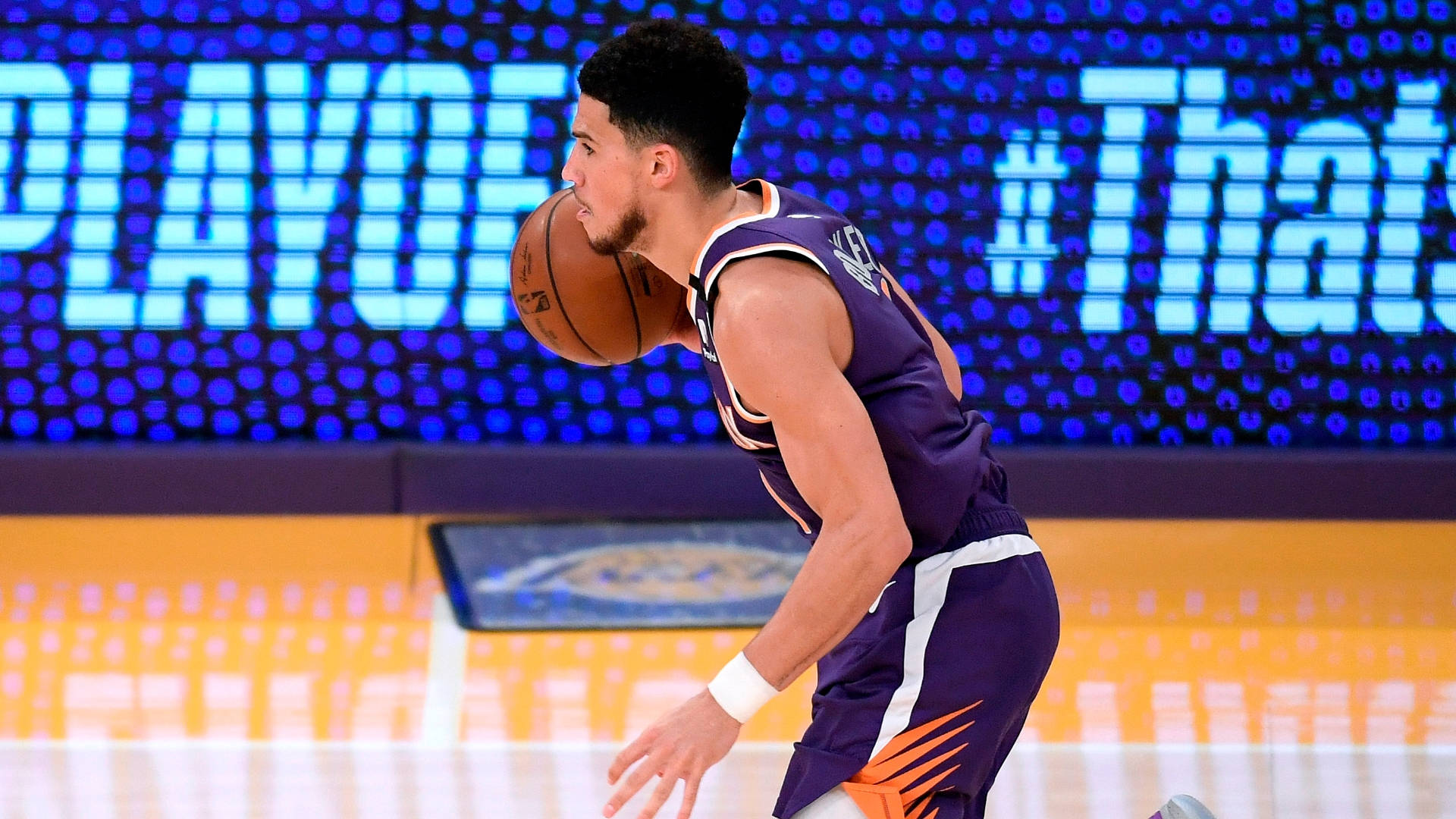 Devin Booker 桌布 壁紙 — 一名身穿紫色球衣的籃球運動員在明亮的場館燈光下，在季後賽比賽中專注地運球。