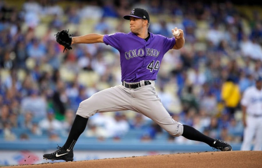 Colorado Rockies 桌布 壁紙 — 一名身穿紫色科羅拉多洛磯隊球衣的棒球投手，在陽光明媚的投手丘上投球，背景是模糊的球場觀眾。
